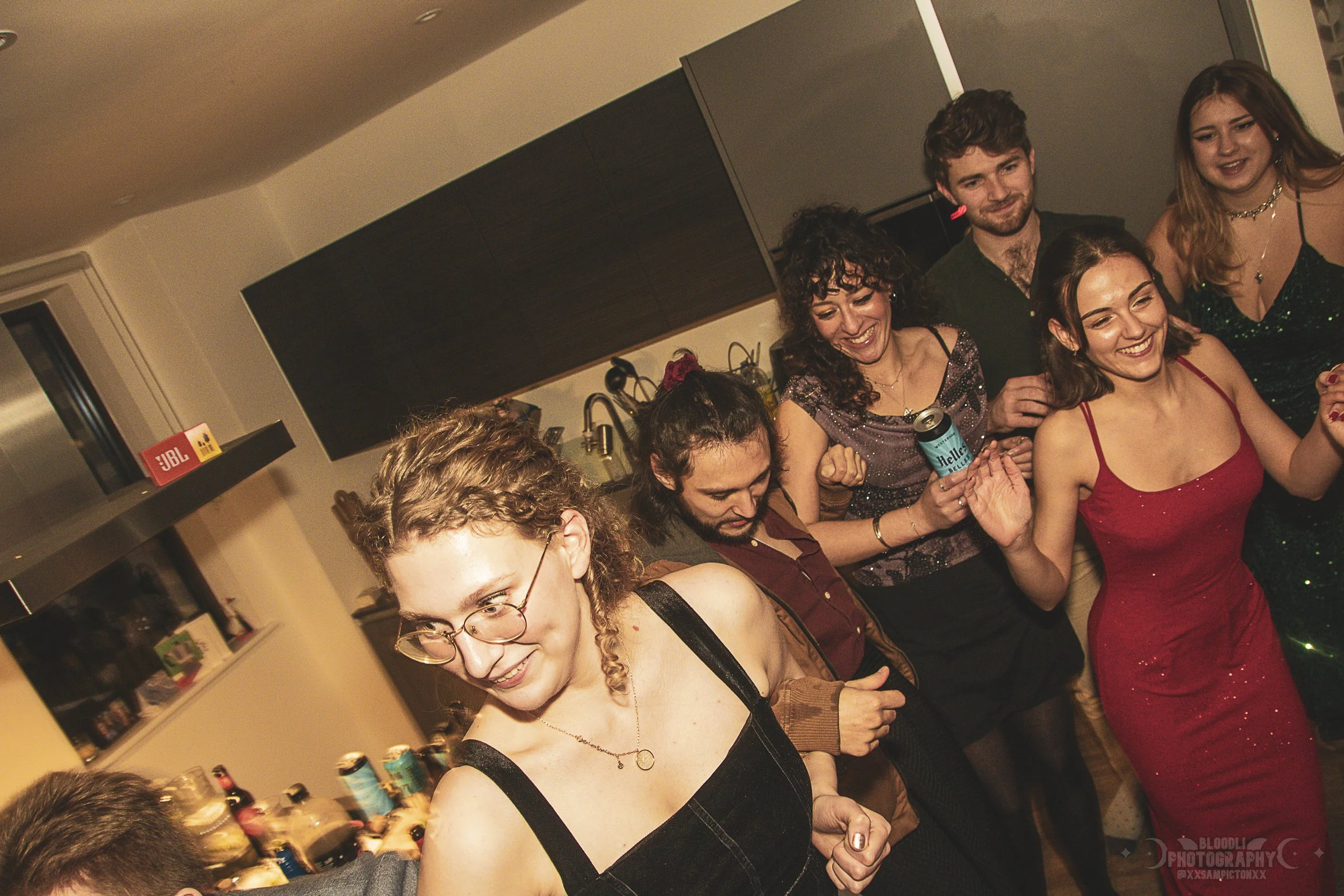 Group of friends at a party dancing and smiling in a kitchen