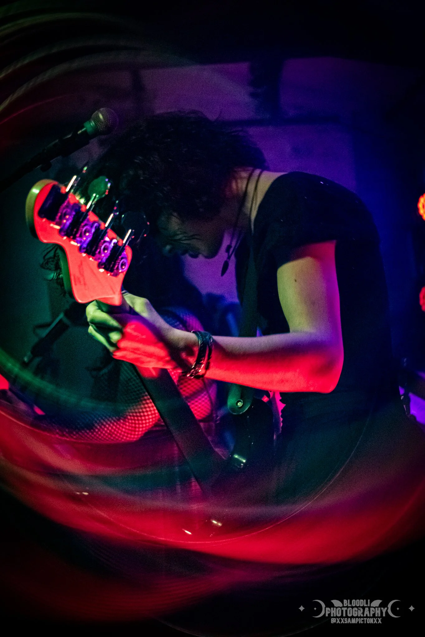 A woman playing an electric guitar on stage with vibrant red, green, blue, and purple stage lights.