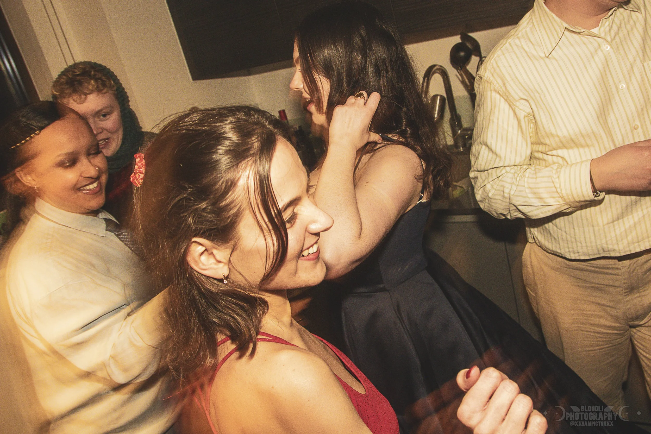 Group of people dancing and laughing at a party in a kitchen.