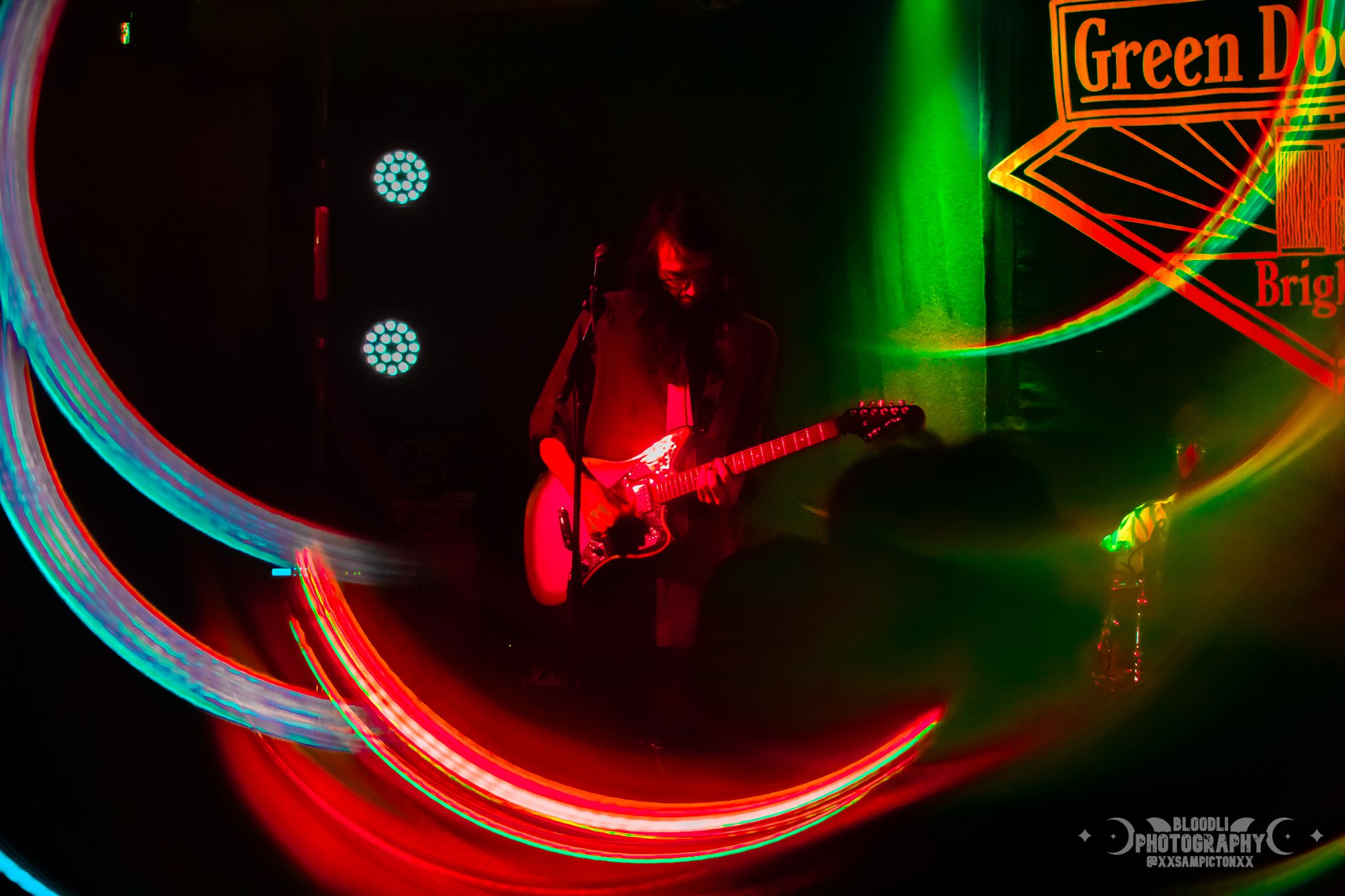 A person playing an electric guitar on a stage with colorful light trails and stage lights in the background.