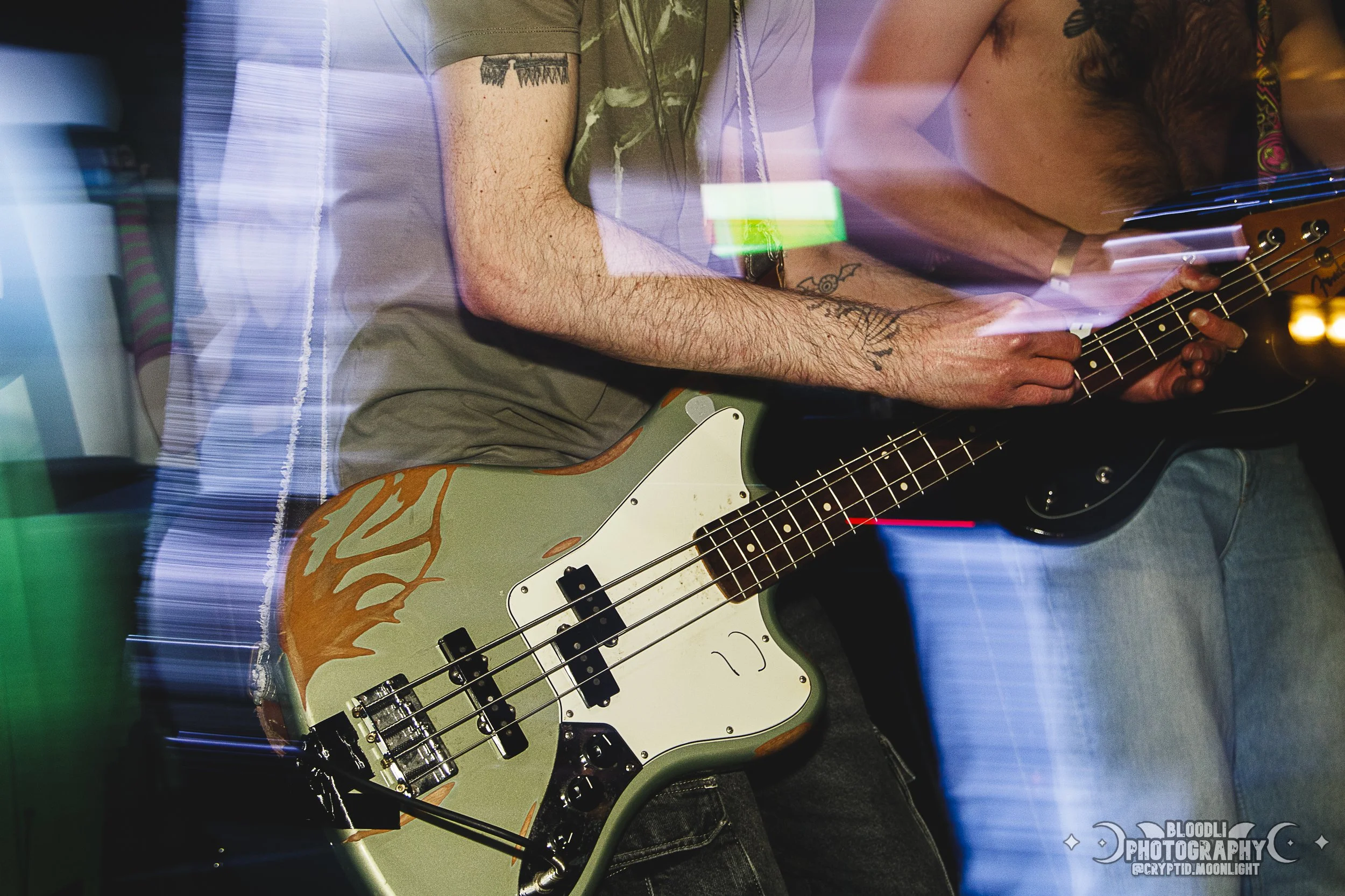 Person playing electric bass guitar at a music event, with light streaks and reflections creating a dynamic atmosphere.