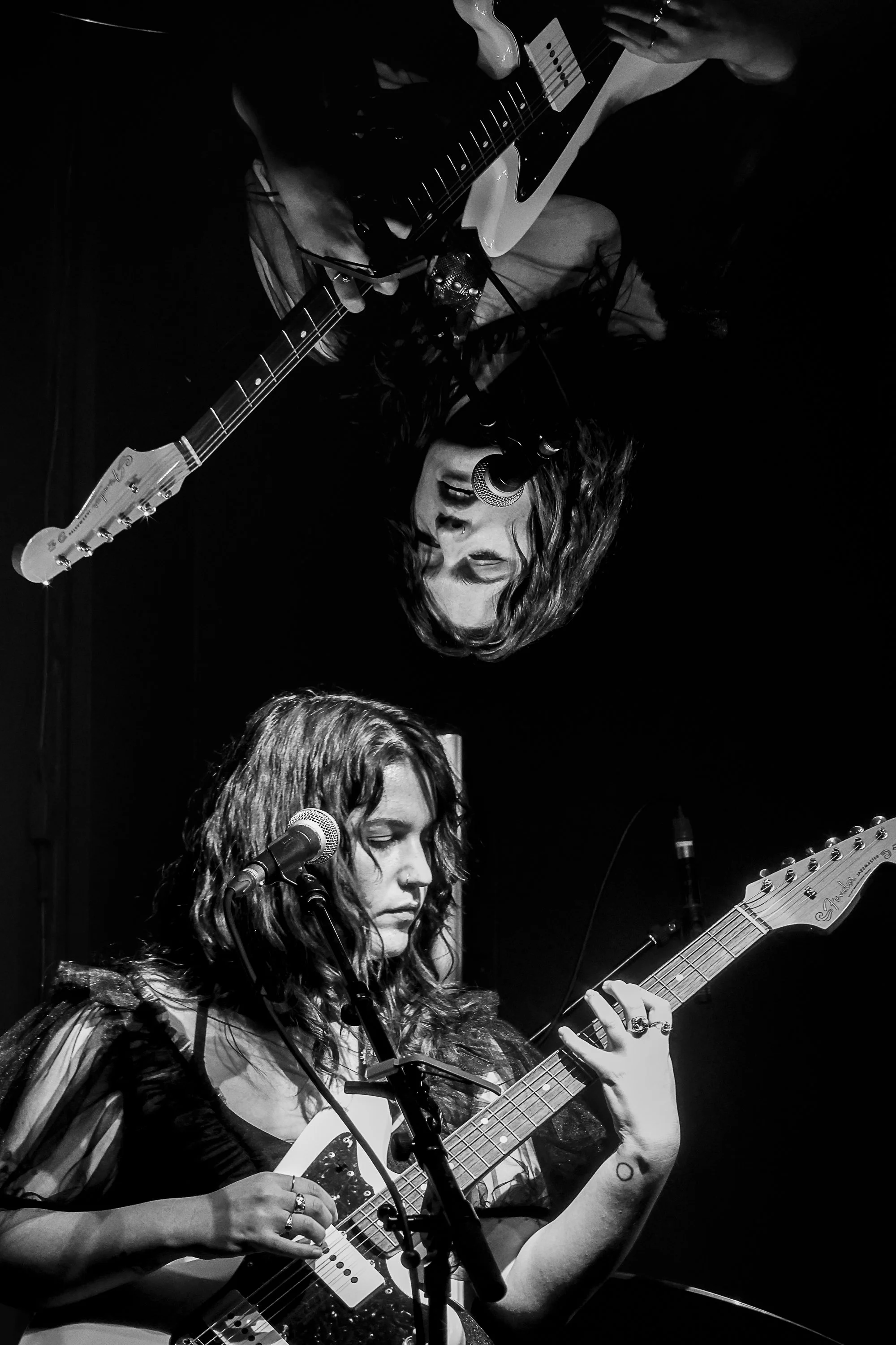 Two women with curly hair performing on stage with guitars and microphones in black and white.