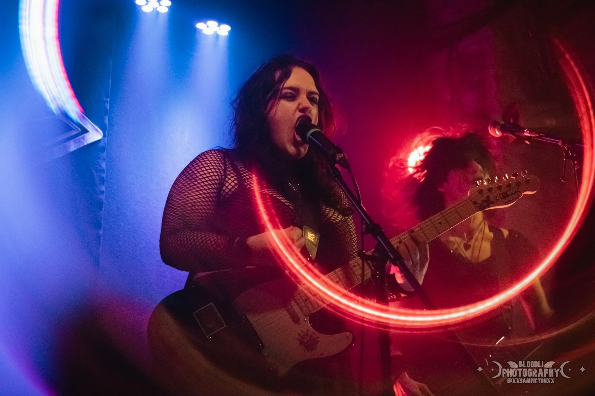 Female musician performing with guitar on stage, surrounded by colorful lights and a red light ring.