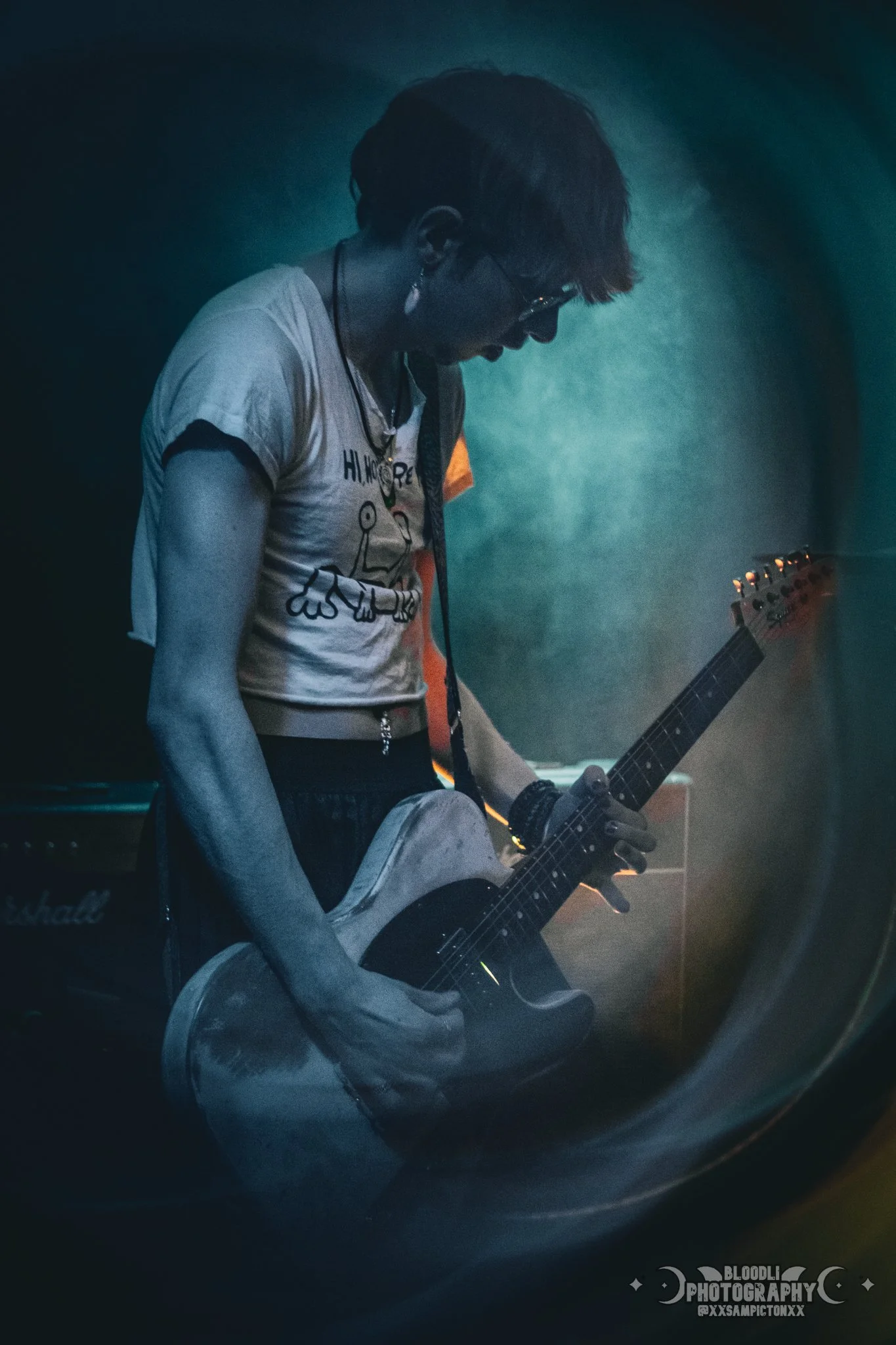 Person playing an electric guitar in a dimly lit room, with a Marshall amplifier in the background.