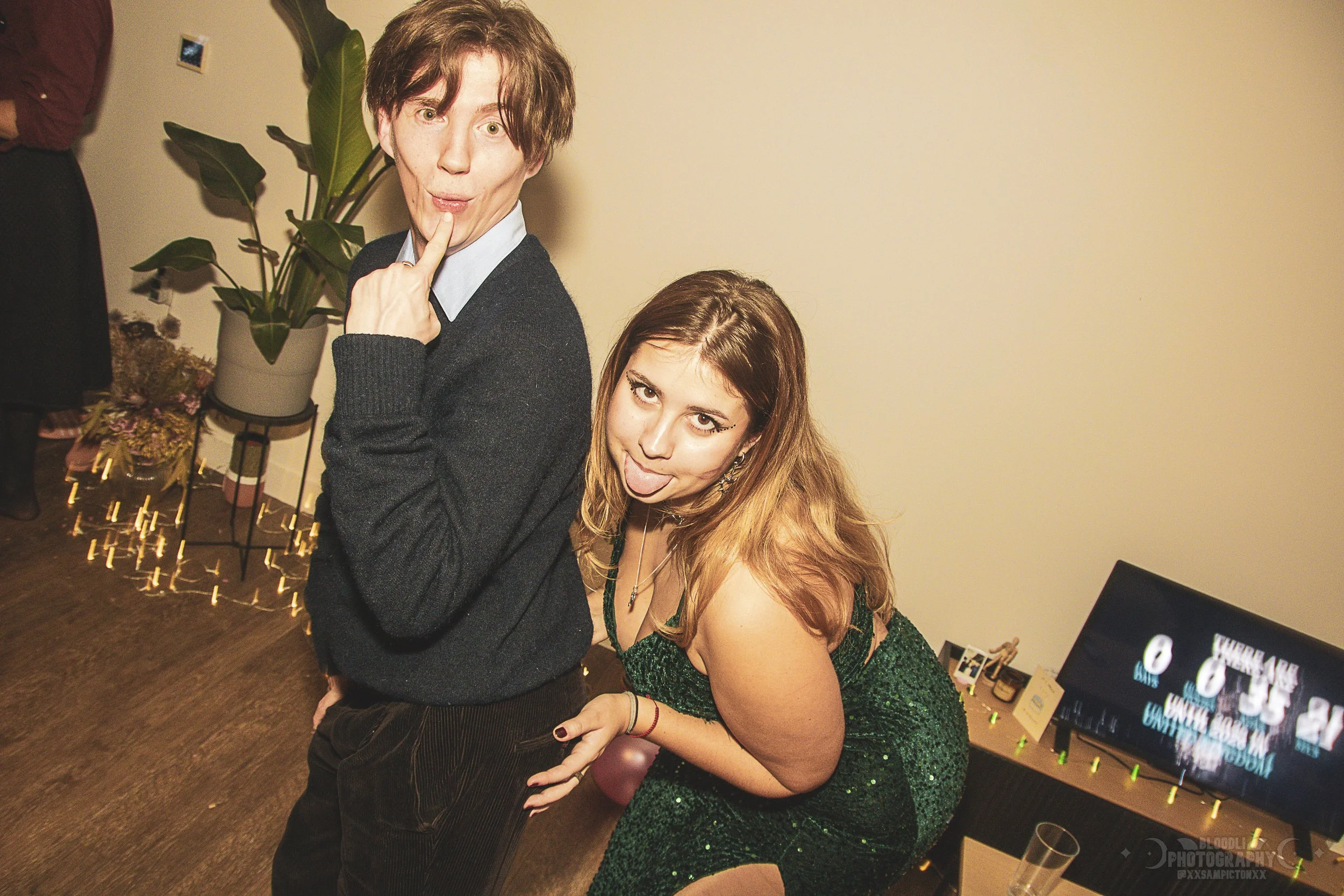 Two young women at a party making silly faces, one standing slightly behind the other, with playful expressions.