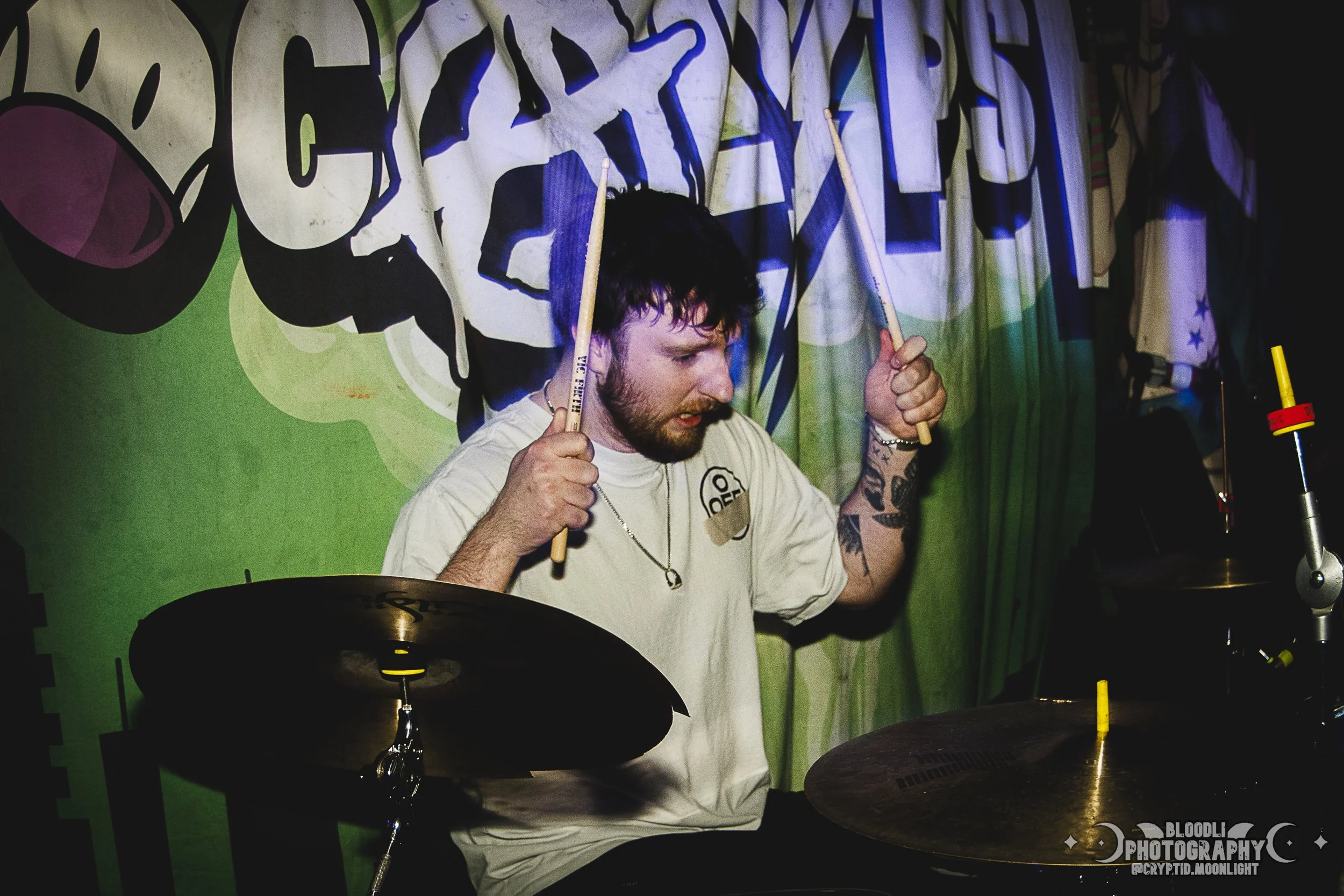 A man playing drums in front of a colorful graffiti backdrop during a live music event.