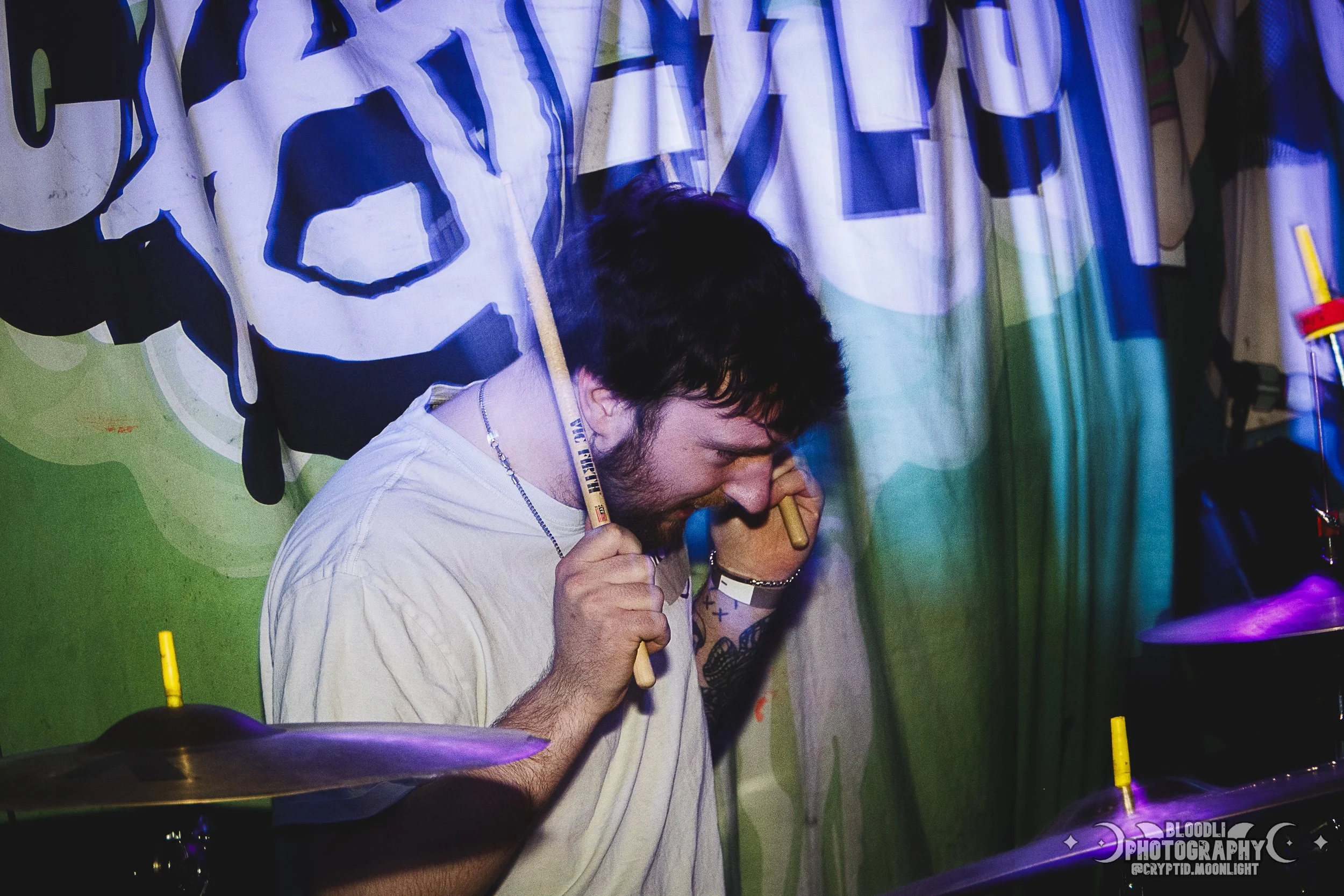 A man playing the drums at a music event with a colorful background.