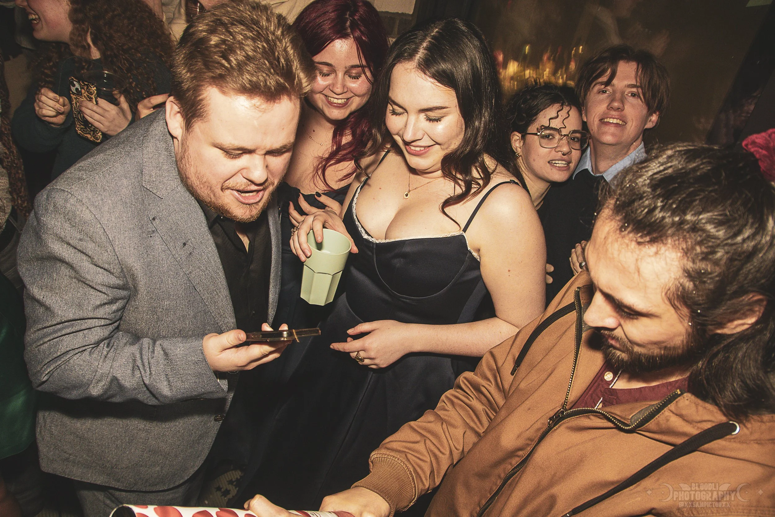 Group of people at a party looking at a phone together, smiling and having fun.