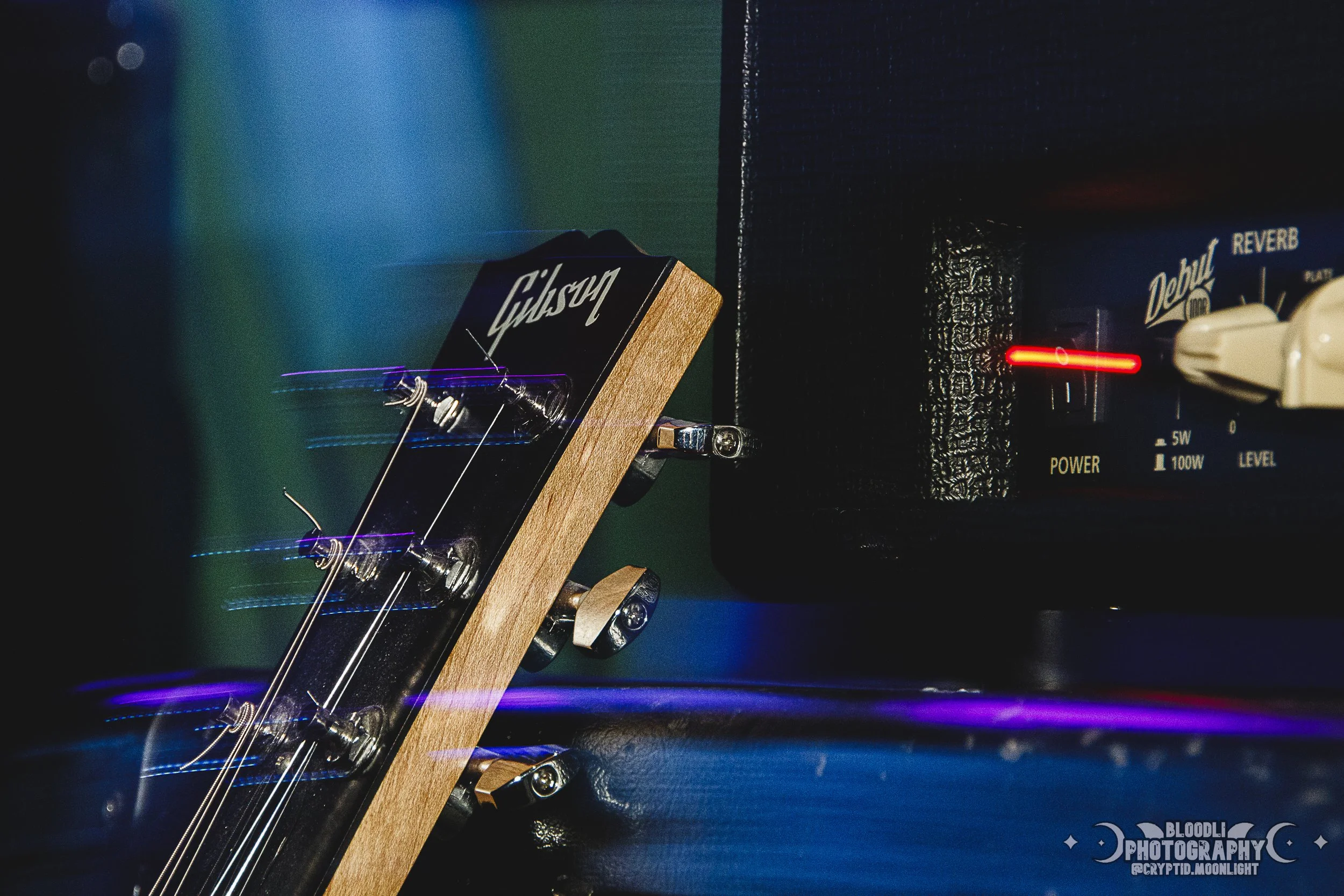 Close-up of a guitar headstock with tuning pegs and strings, next to an amplifier with glowing power indicator and a reverb knob.