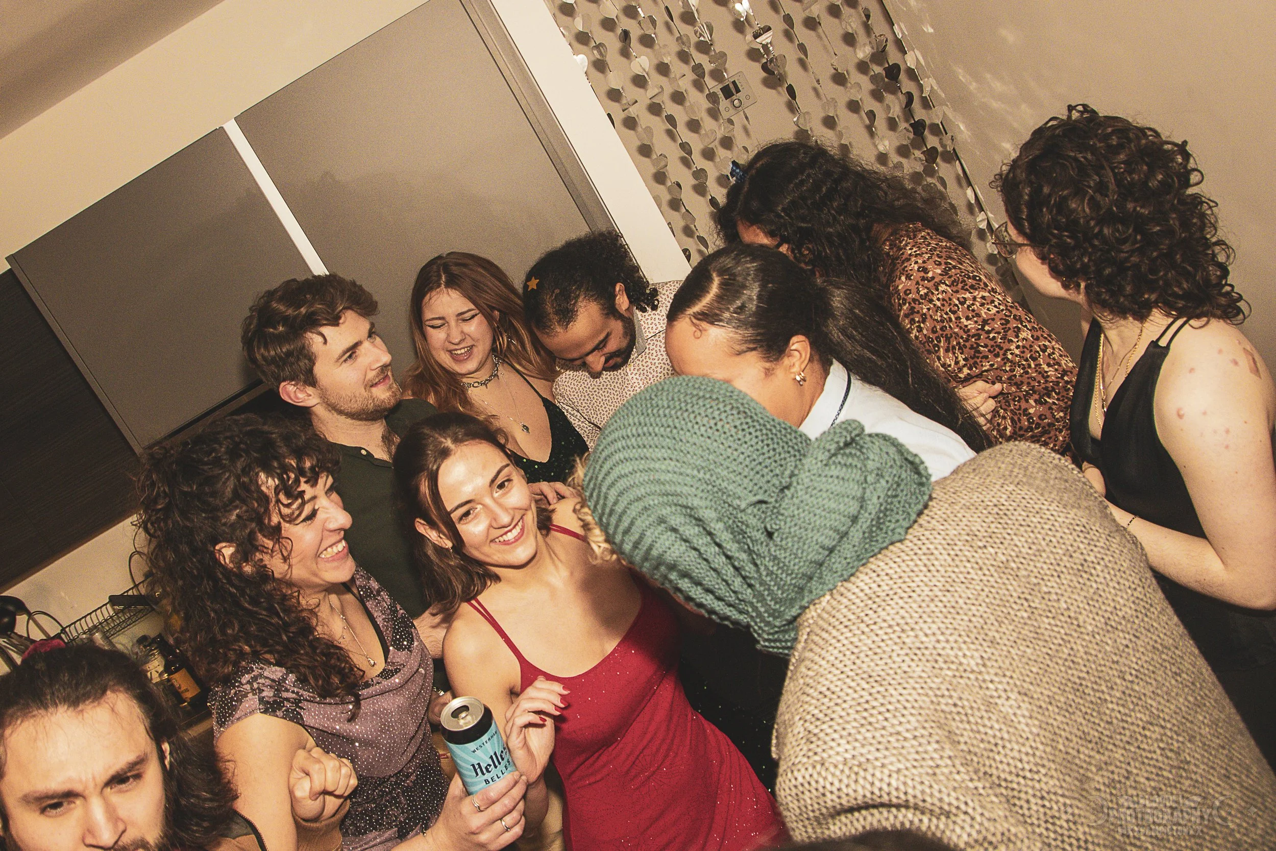 Group of people gathered together at a party, smiling and talking with each other, some holding drinks.