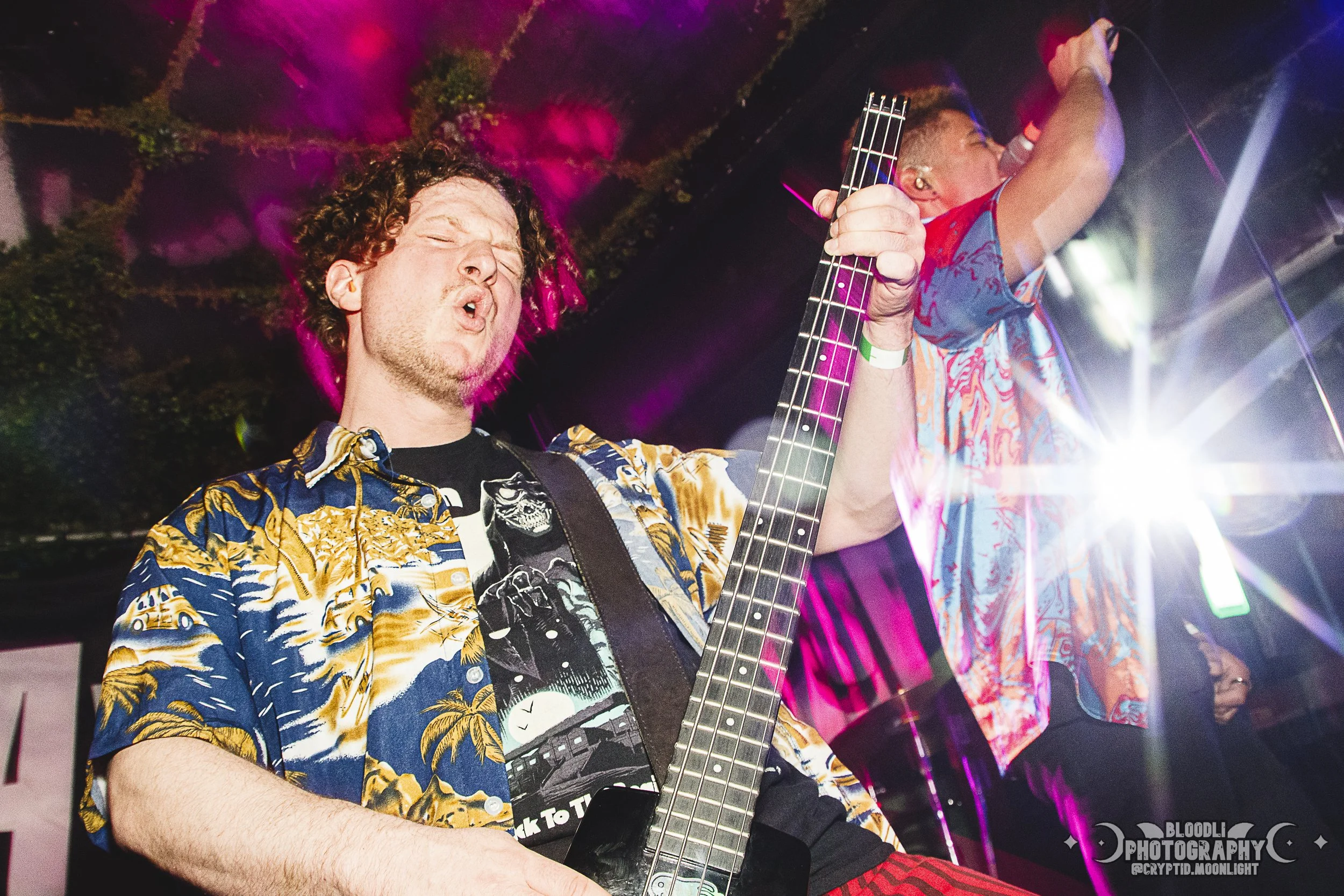 Two musicians performing on stage, with one playing an electric guitar and the other singing into a microphone. The stage is lit with colorful lights, creating a vibrant atmosphere.