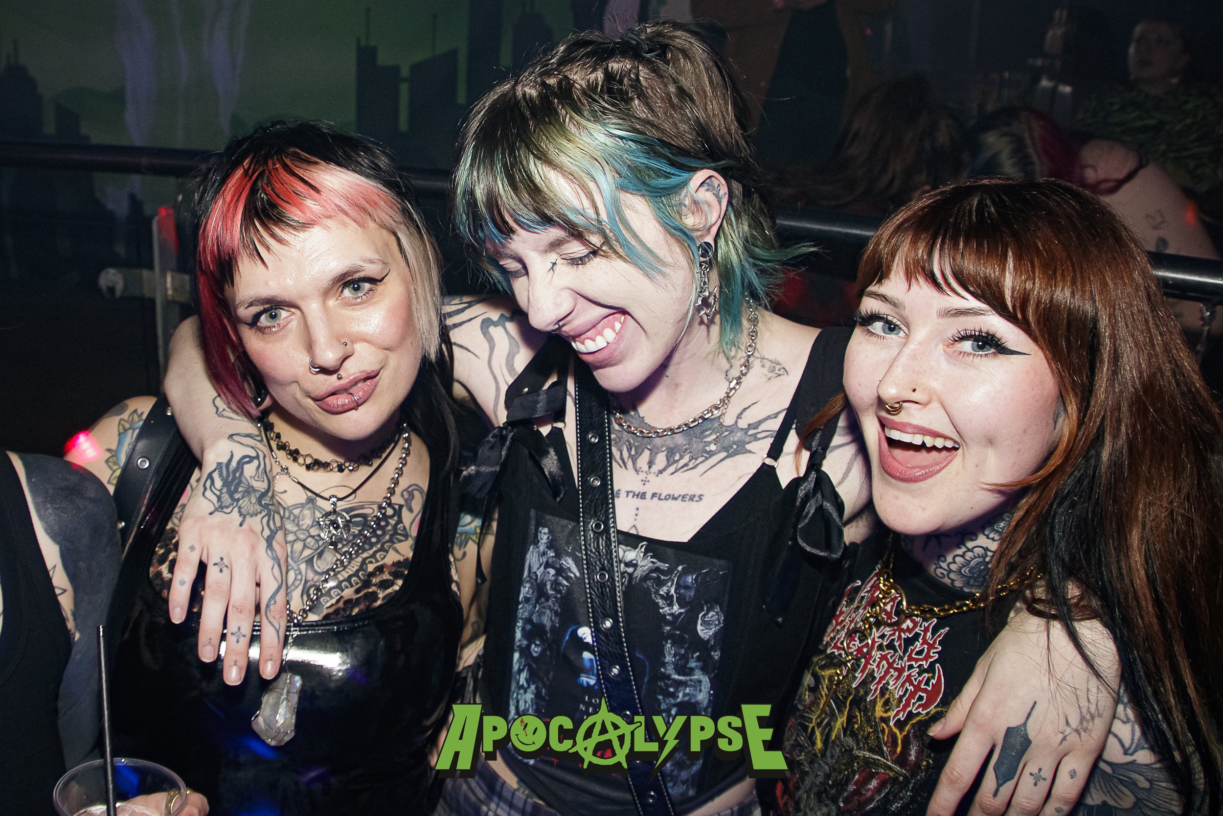 Three women with tattoos and piercings smiling and enjoying themselves at a party or club, with the name 'Apocalypse' in green text at the bottom.