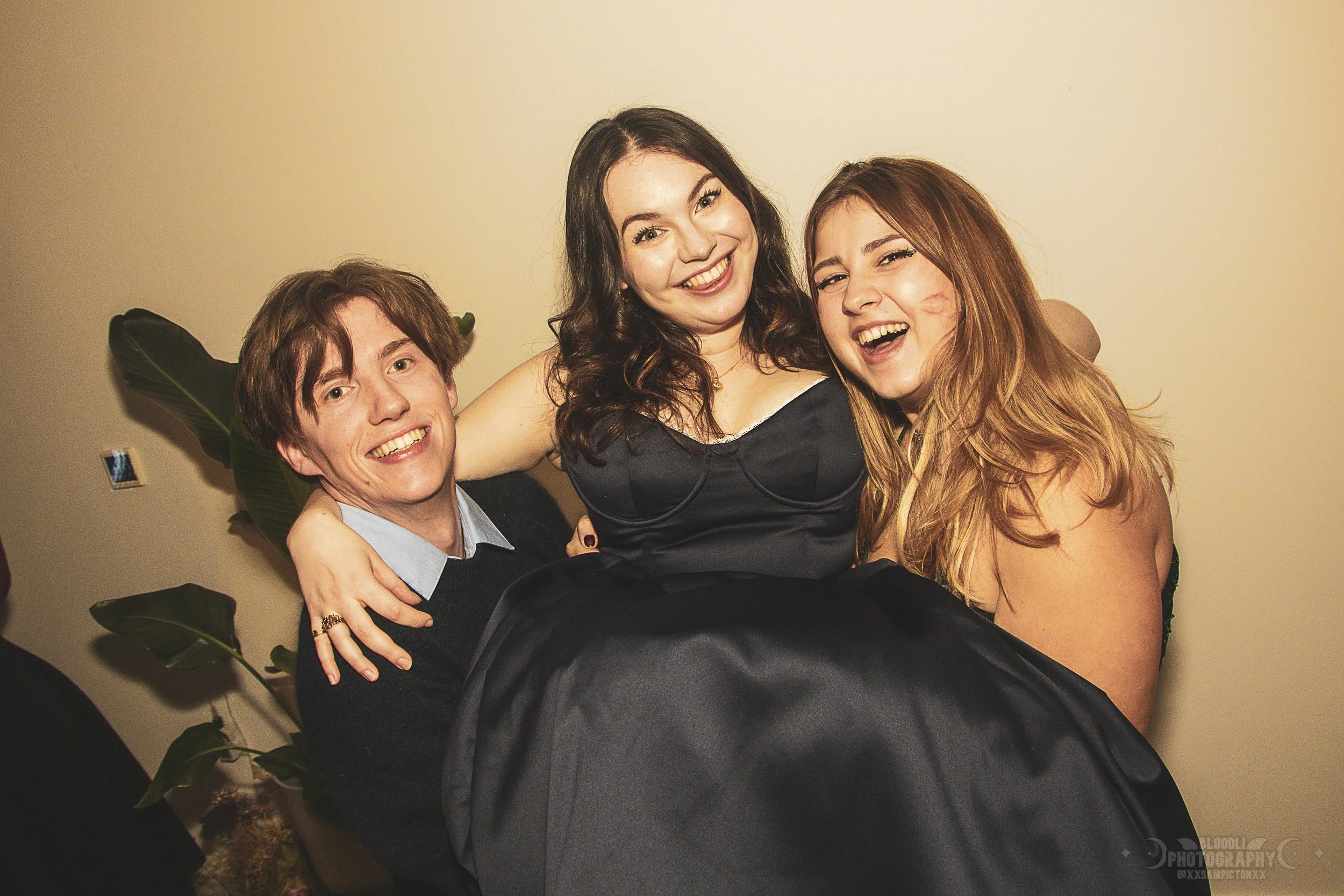 Three friends smiling and celebrating together, one carrying another in a festive setting.