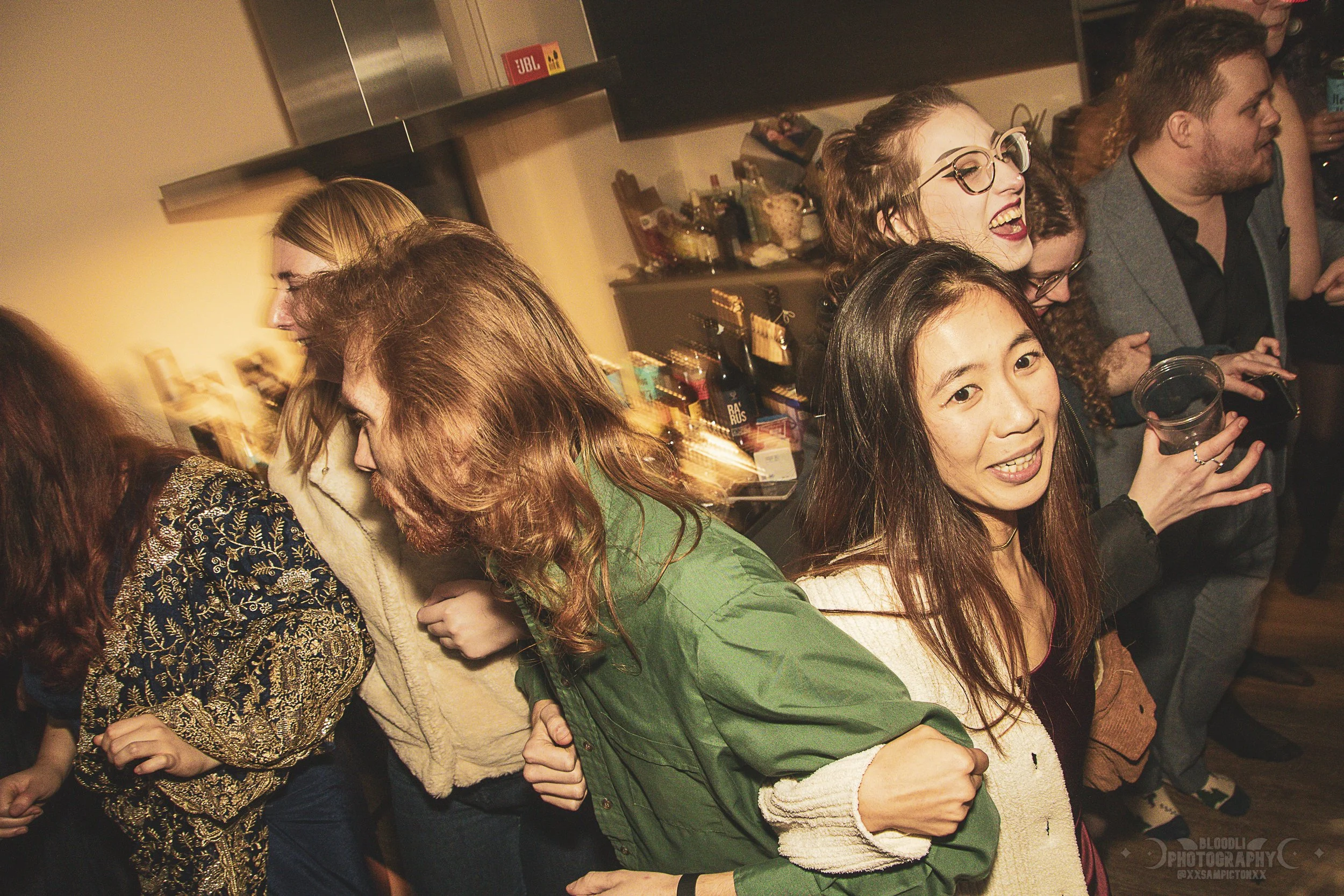 Group of people at a party, dancing and smiling in a cozy indoor setting.