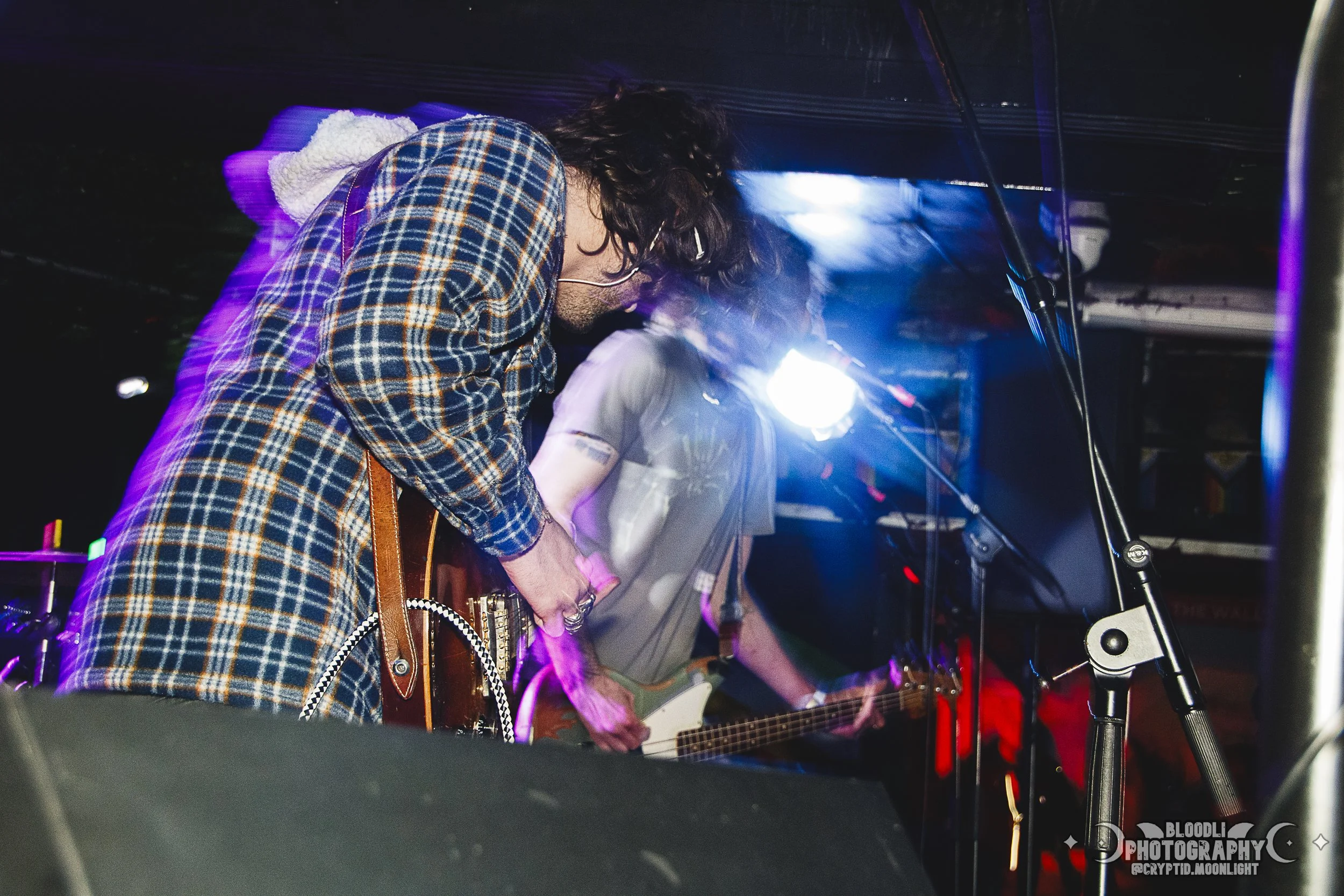 Musicians performing on stage, playing guitars, with colorful stage lighting and microphones.