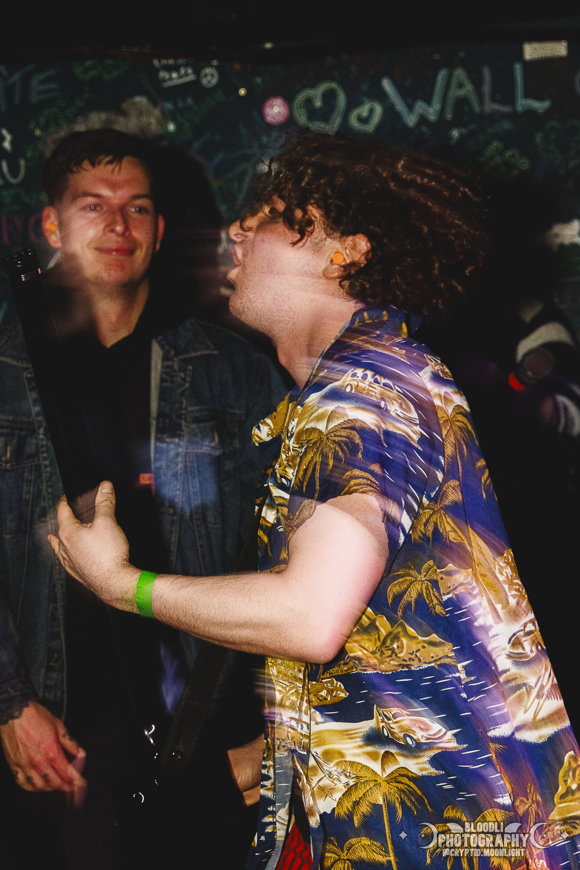 Two men exchanging a fist bump in a lively, colorful environment with a chalkboard background.