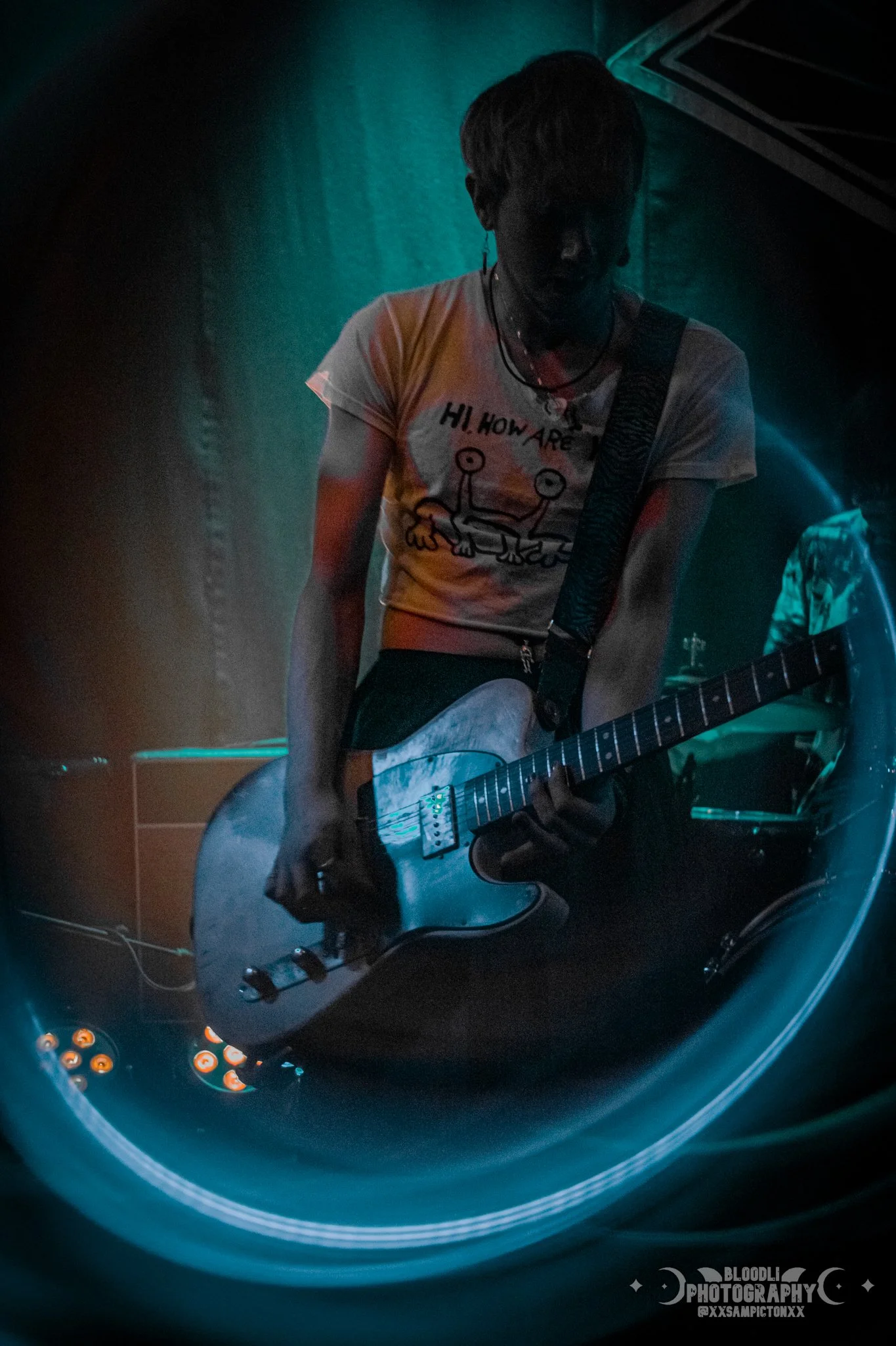 Person playing a guitar on stage with colorful lighting.