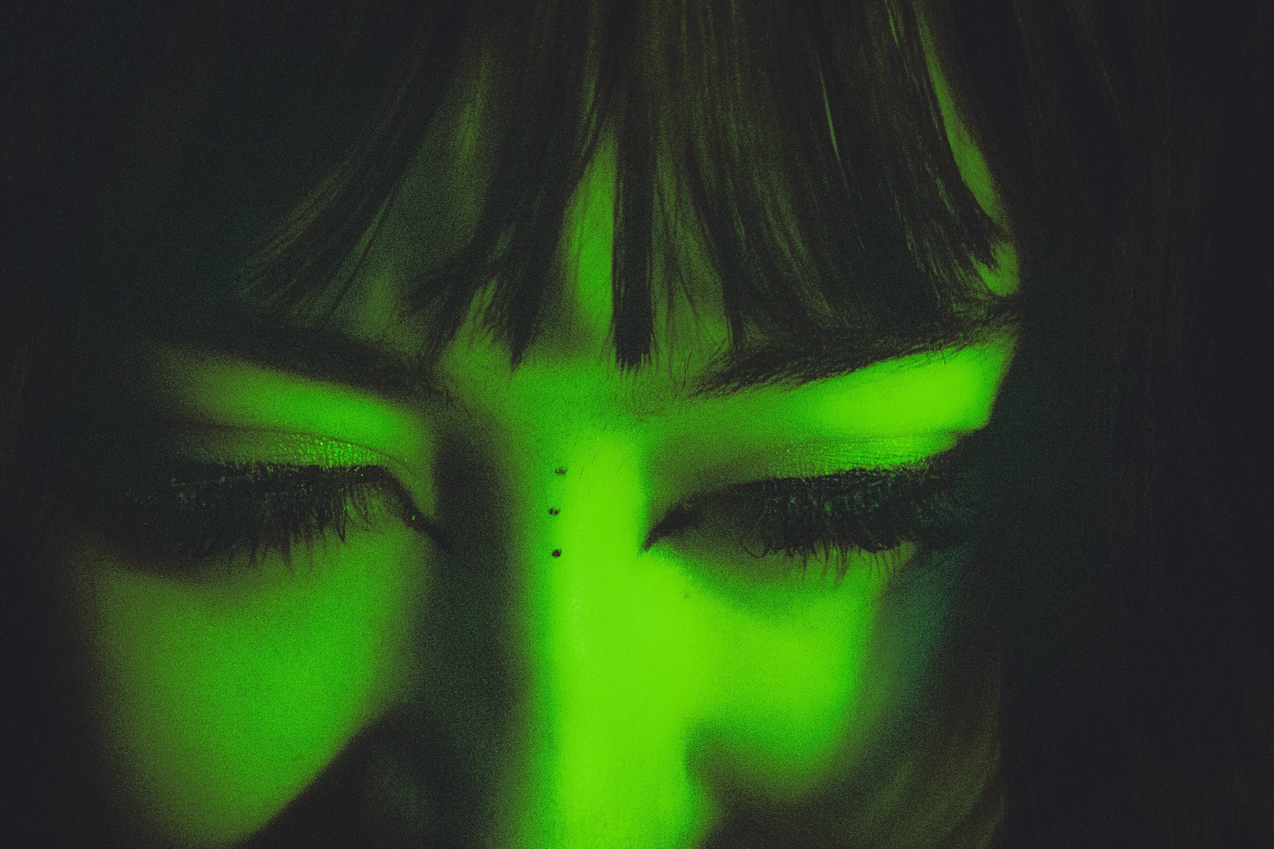 Close-up of a person's face illuminated by green light, focusing on closed eyes and long eyelashes.