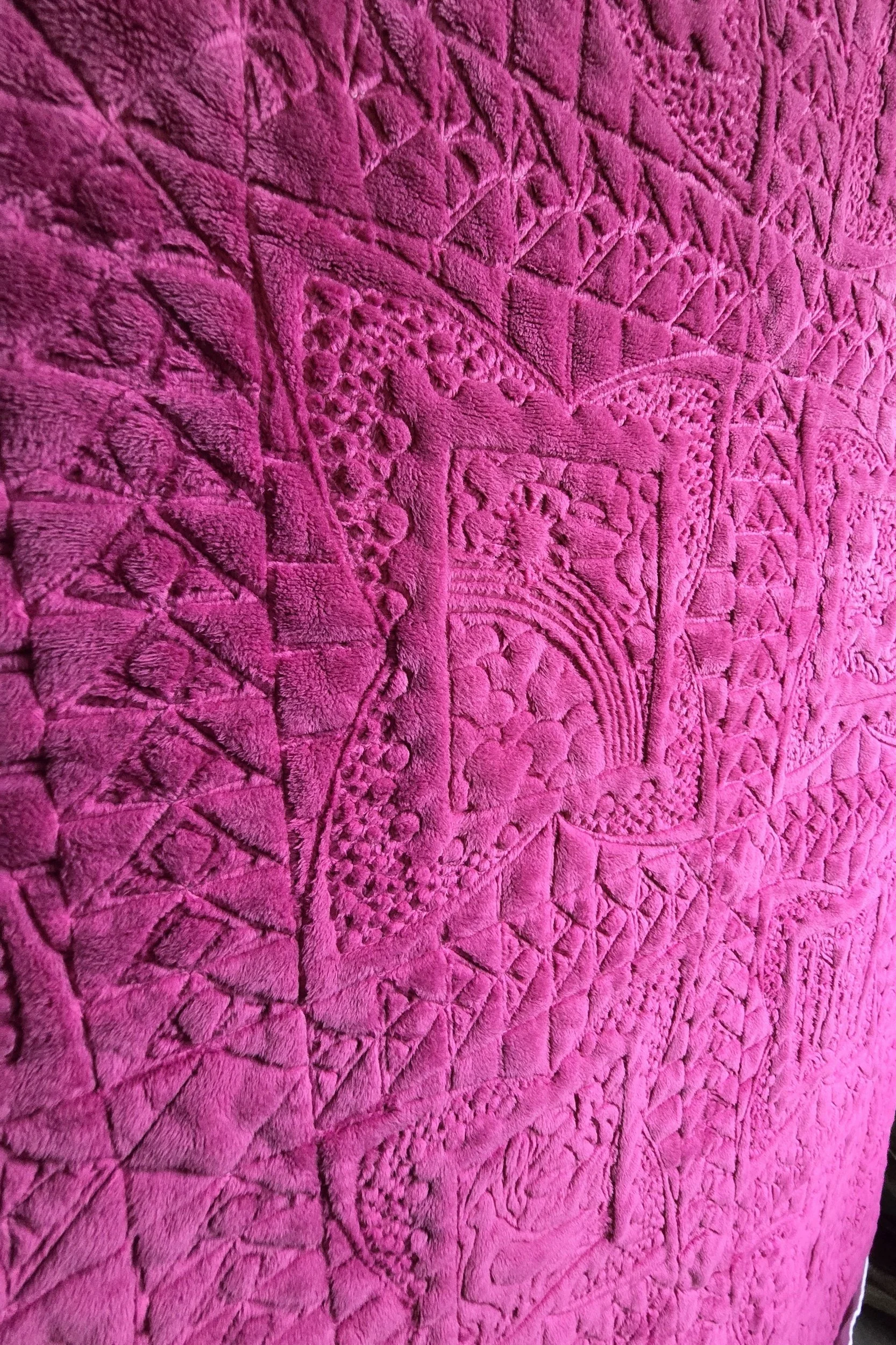 Close-up of a bright pink textured quilt with intricate stitched patterns.