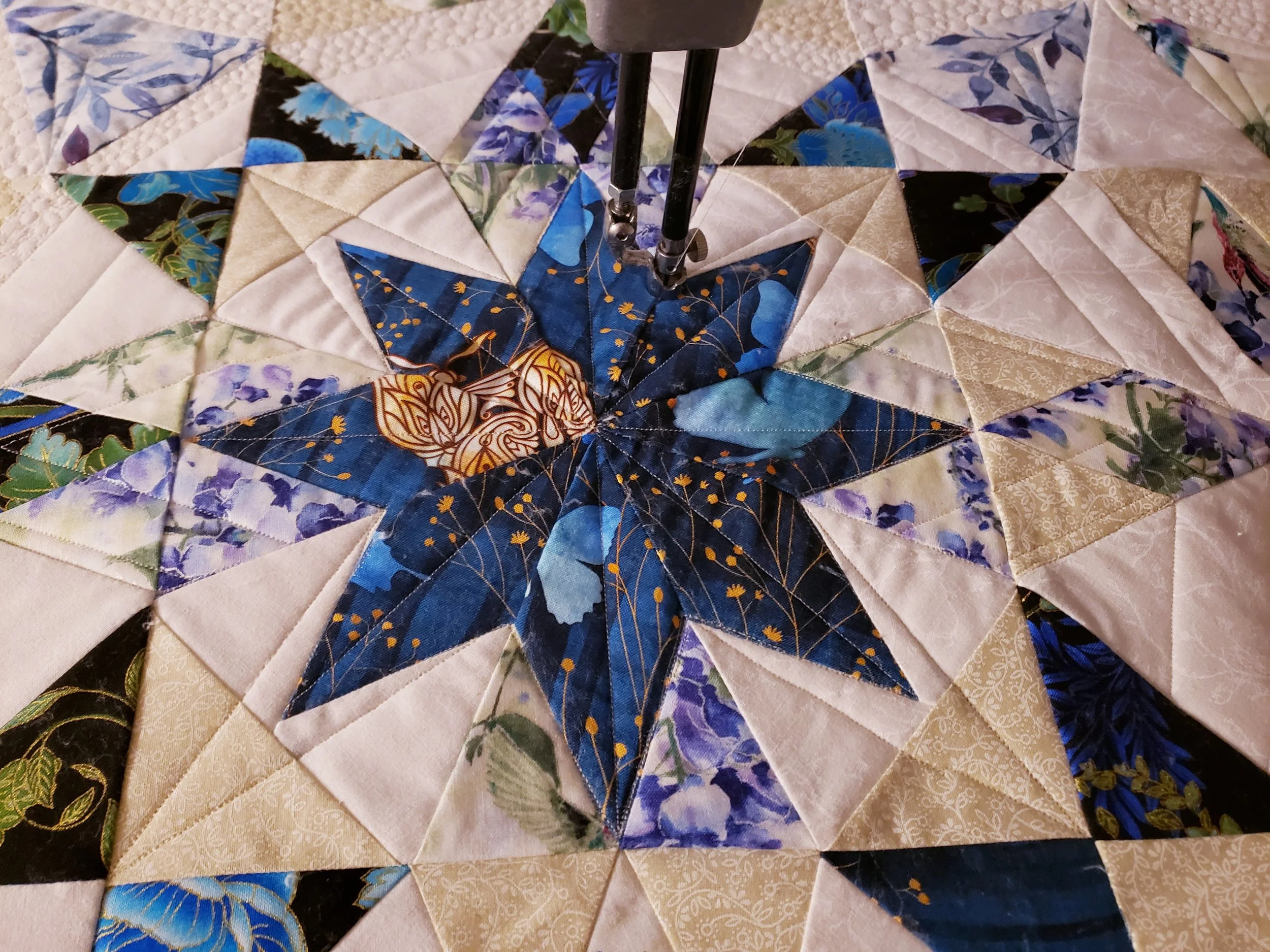 Close-up of a colorful quilt featuring a star pattern with various floral fabrics in shades of blue, beige, white, and black.