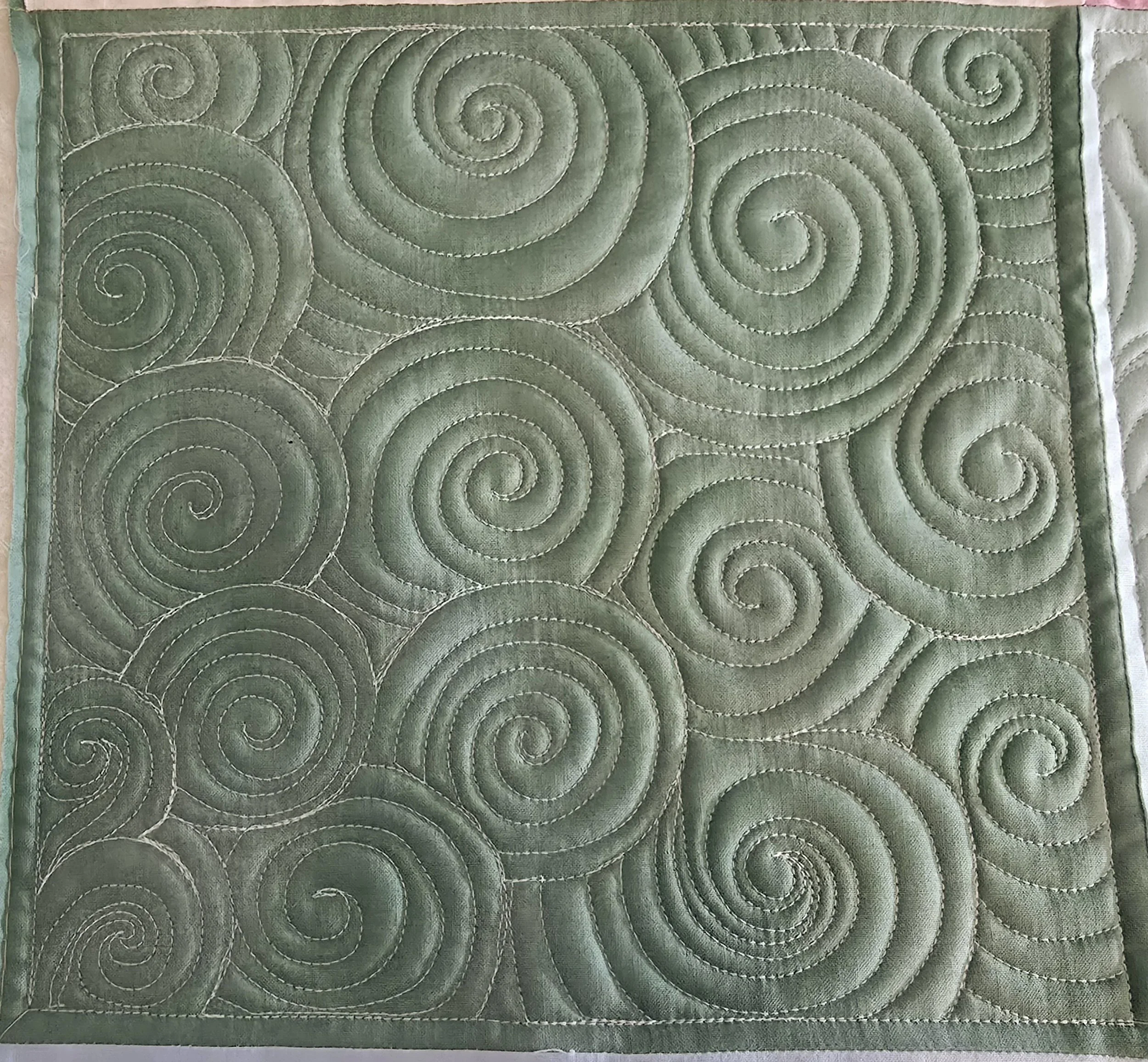 Close-up of a green quilt with swirling stitch patterns.