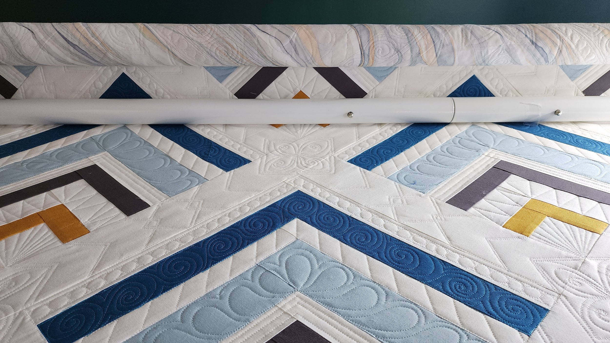 A colorful quilt with geometric patterns and quilting details, with a metal pole running across the center.