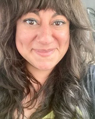 Close-up of a woman with long wavy brown hair and light skin, smiling and looking at the camera.