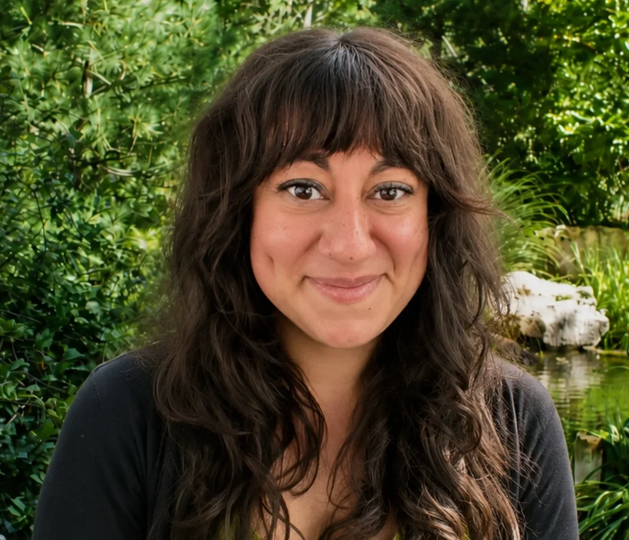 Close-up of a woman with long wavy brown hair and light skin, smiling and looking at the camera.