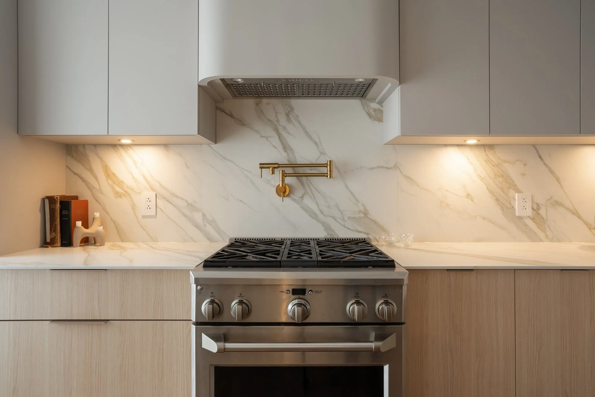 Cuisine moderne avec comptoir en marbre blanc, décors minimalistes, plaque de cuisson en acier inoxydable, évier noir, et des armoires gris clair suspendues.