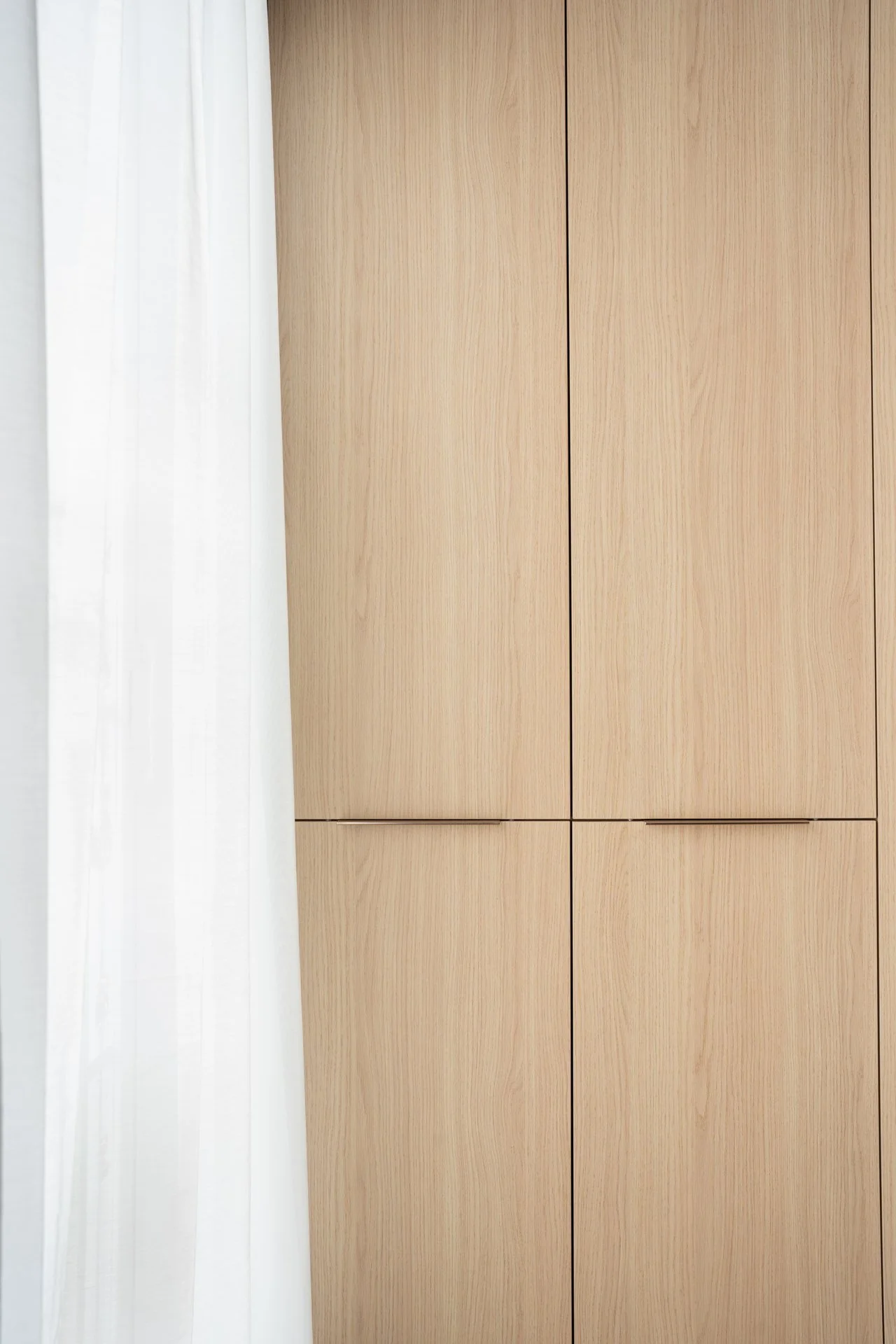 Placard en bois clair avec quatre portes, partiellement couvert par un rideau blanc
