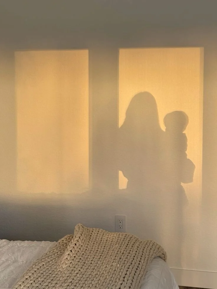 Shadow of a woman and child cast on a wall, with sunlight coming through two windows