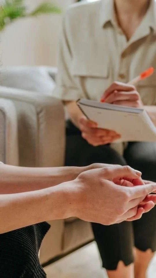 Two people holding hands during a consultation, with one person writing notes in a notebook.