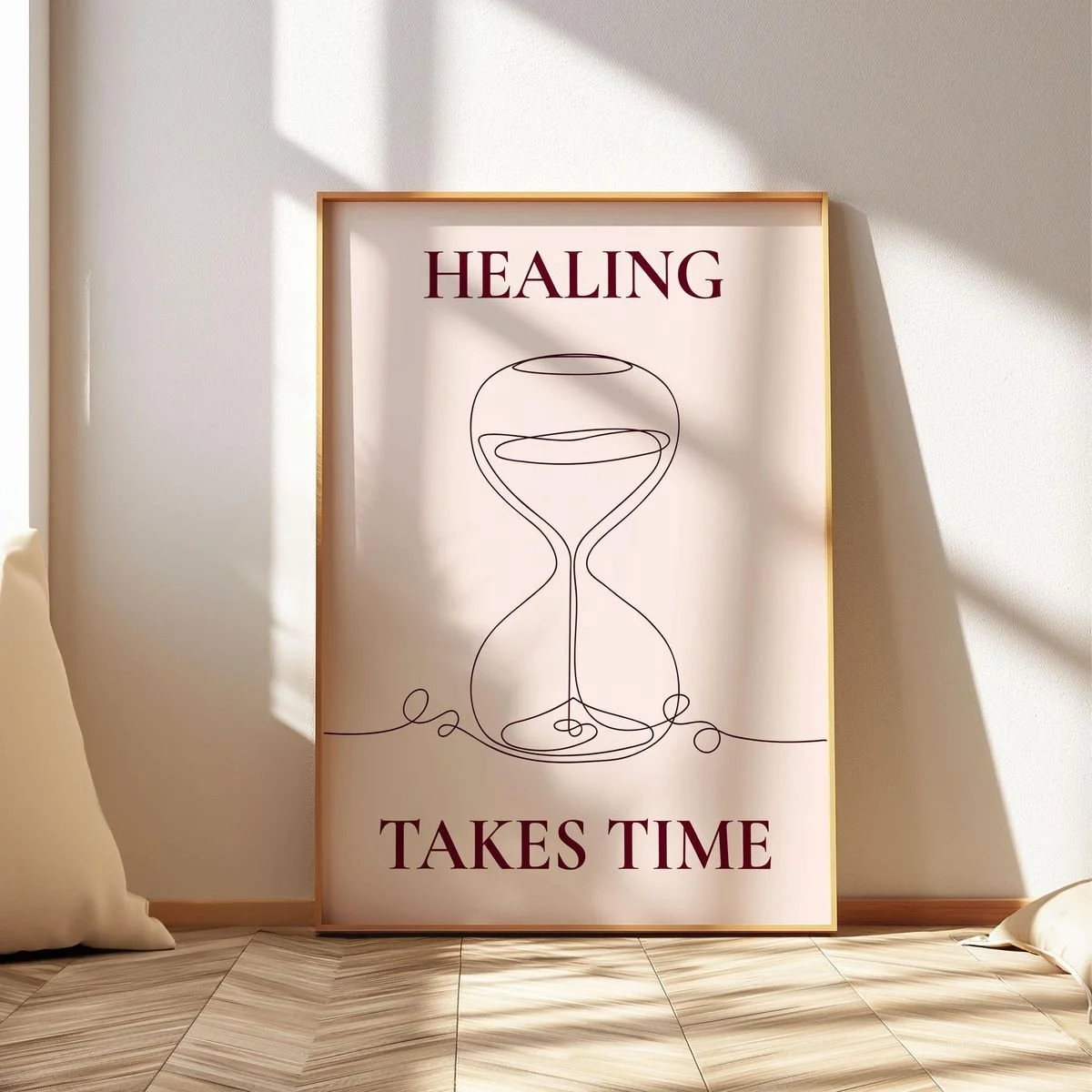Framed poster on a wall with the words "Healing Takes Time" and a minimalistic line drawing of an hourglass, sunlight casting shadows.
