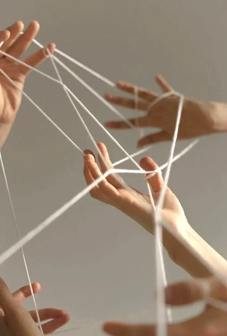 Multiple hands are tangled in white strings, creating a web-like structure.