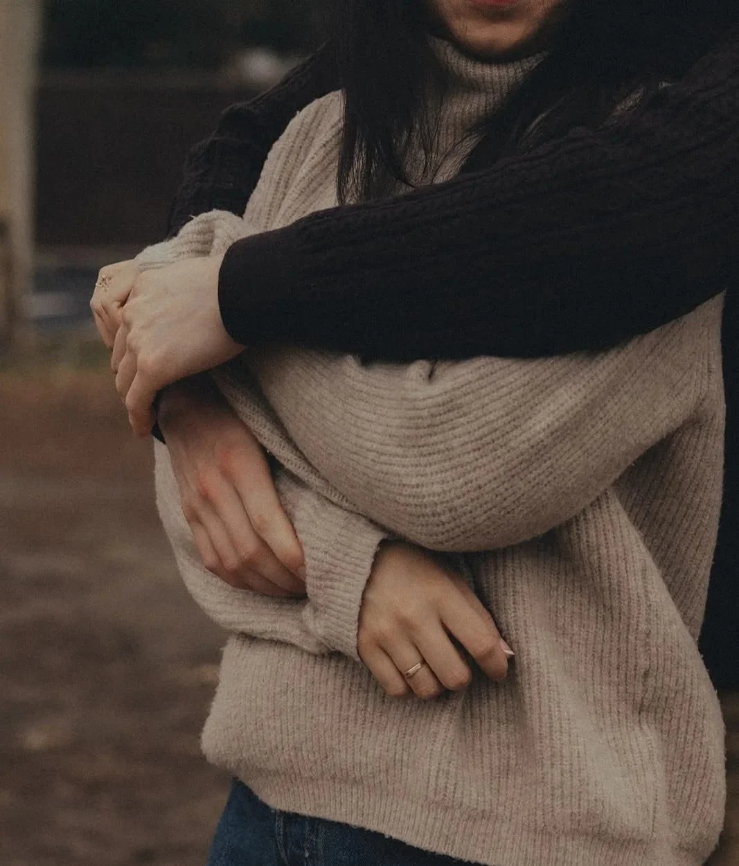 A couple hugging outdoors, wearing warm sweaters during a cold day.