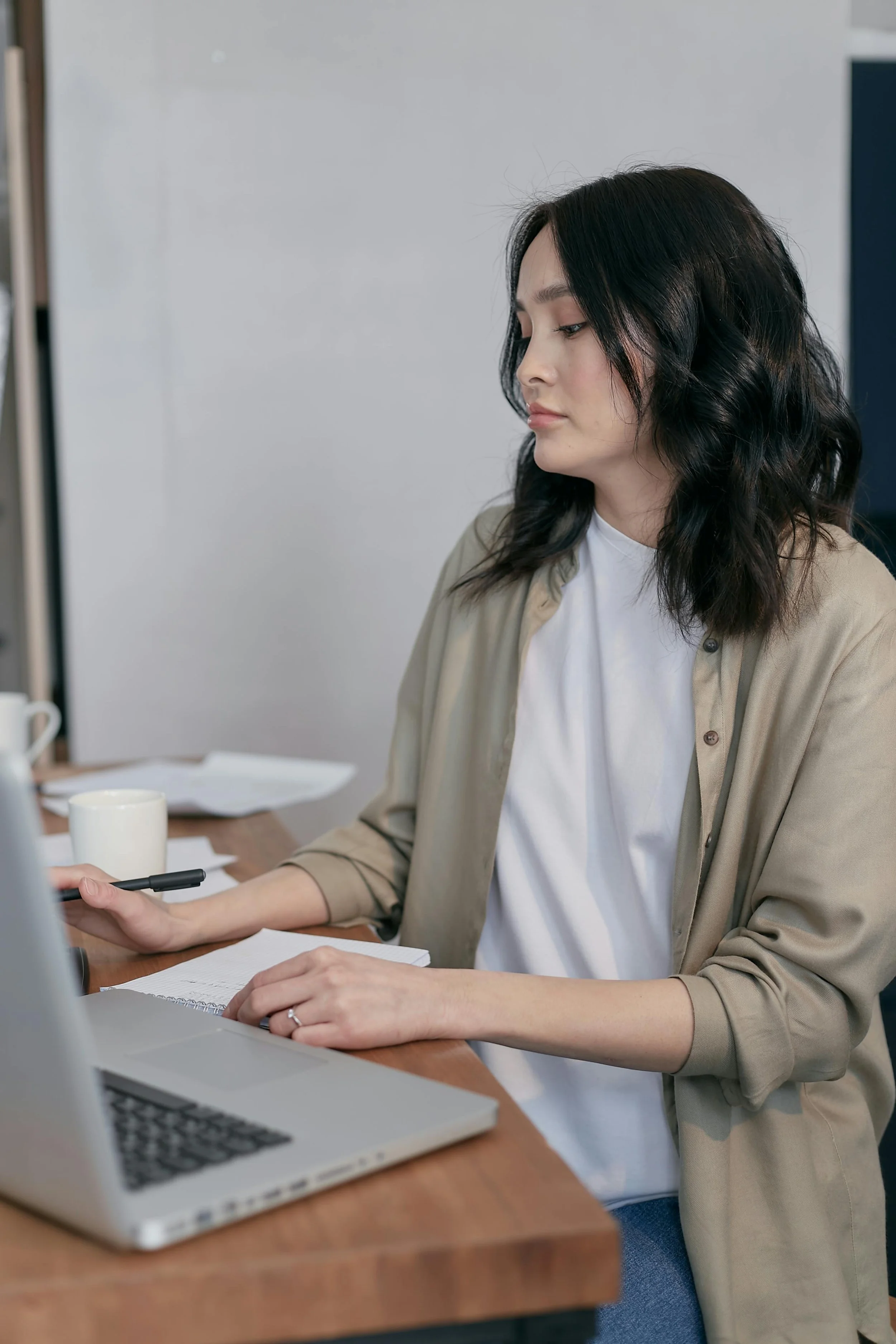 Woman working at a desk with a laptop, notepad, and pen in an office setting.