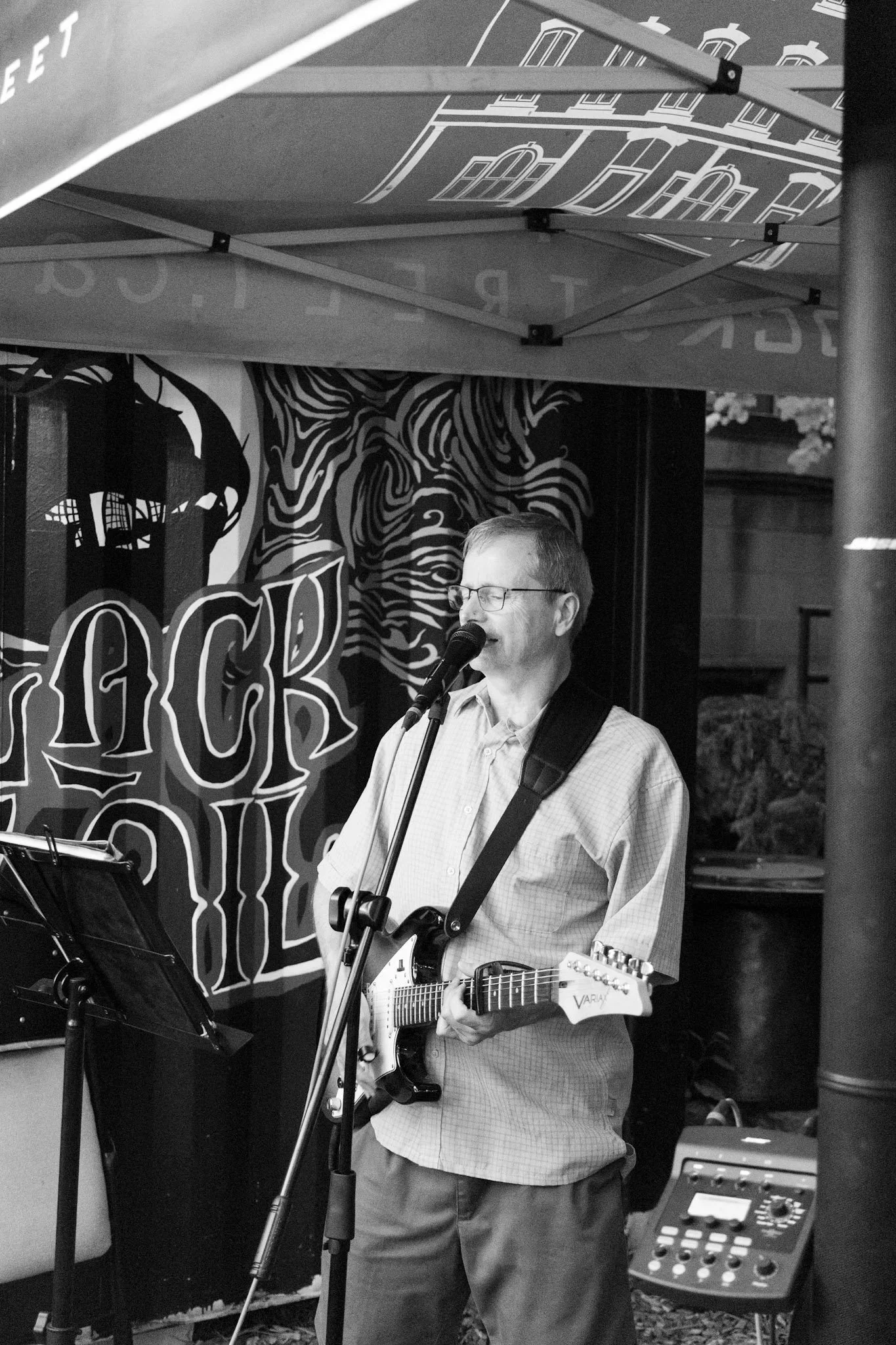 A man with glasses holding a guitar singing into a microphone during a performance at a music venue.