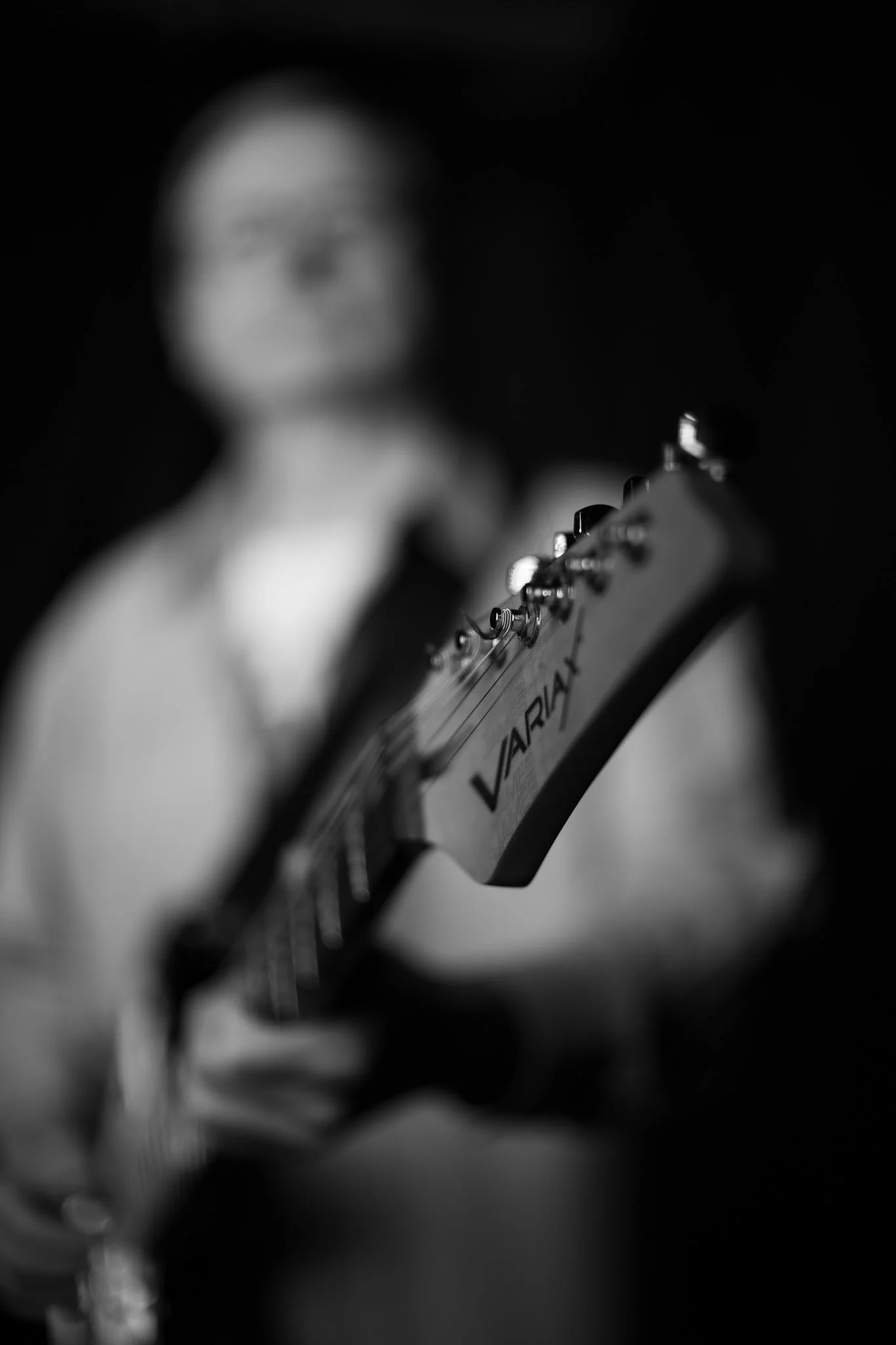 Blurred person playing an electric guitar with focus on the guitar headstock.