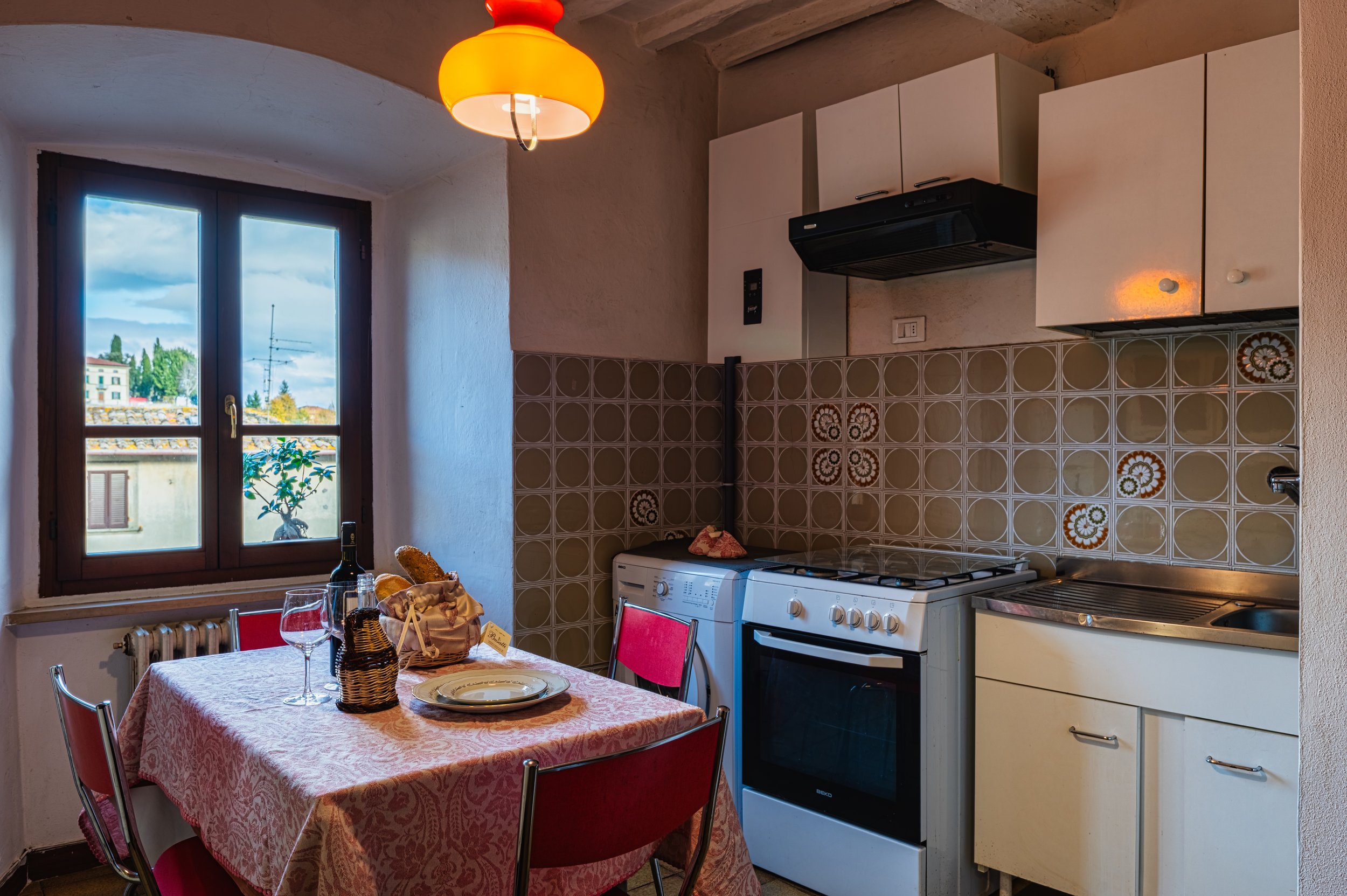 Interno di una cucina con tavolo apparecchiato, forno, frigorifero e soffitto con lampada arancione