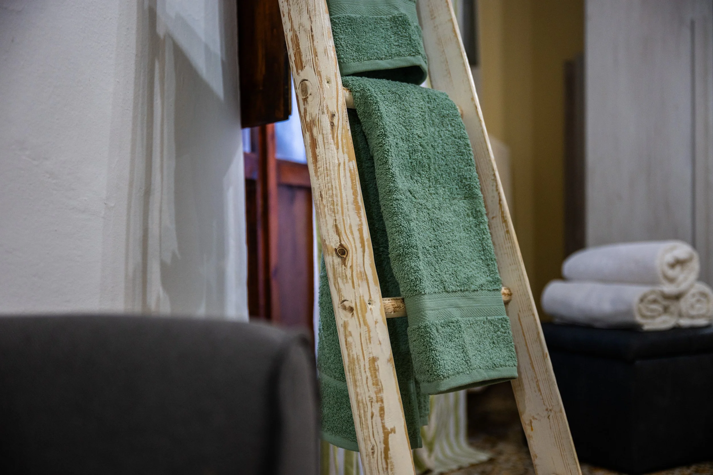 Una scala di legno con asciugamani verdi appesi, in un ambiente domestico con pareti chiare e un mobile in legno.