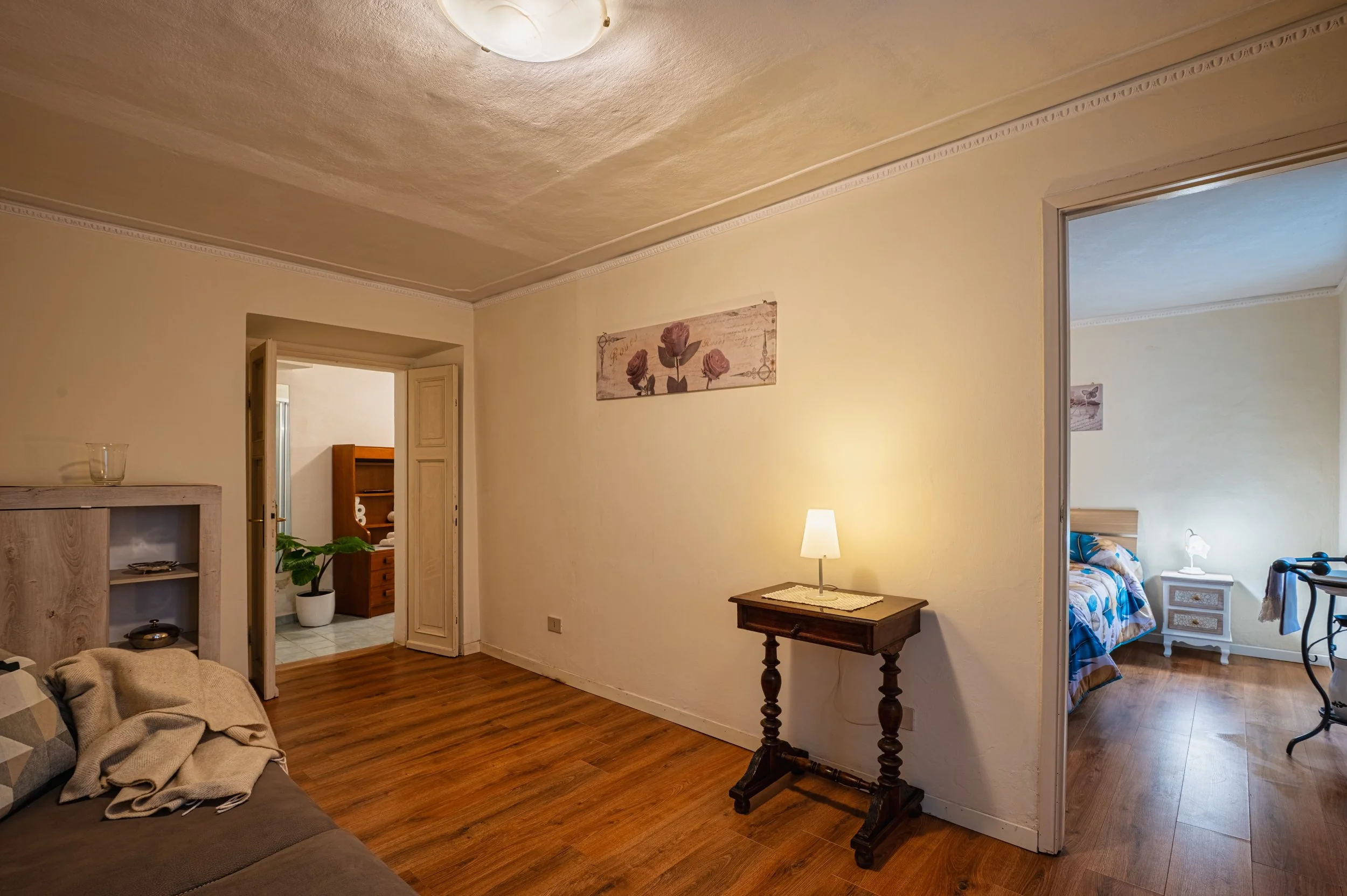 Soggiorno con pareti beige e pavimento in legno, con ingresso alla camera da letto e al bagno, mobili di legno e una sedia con tende in bagno.