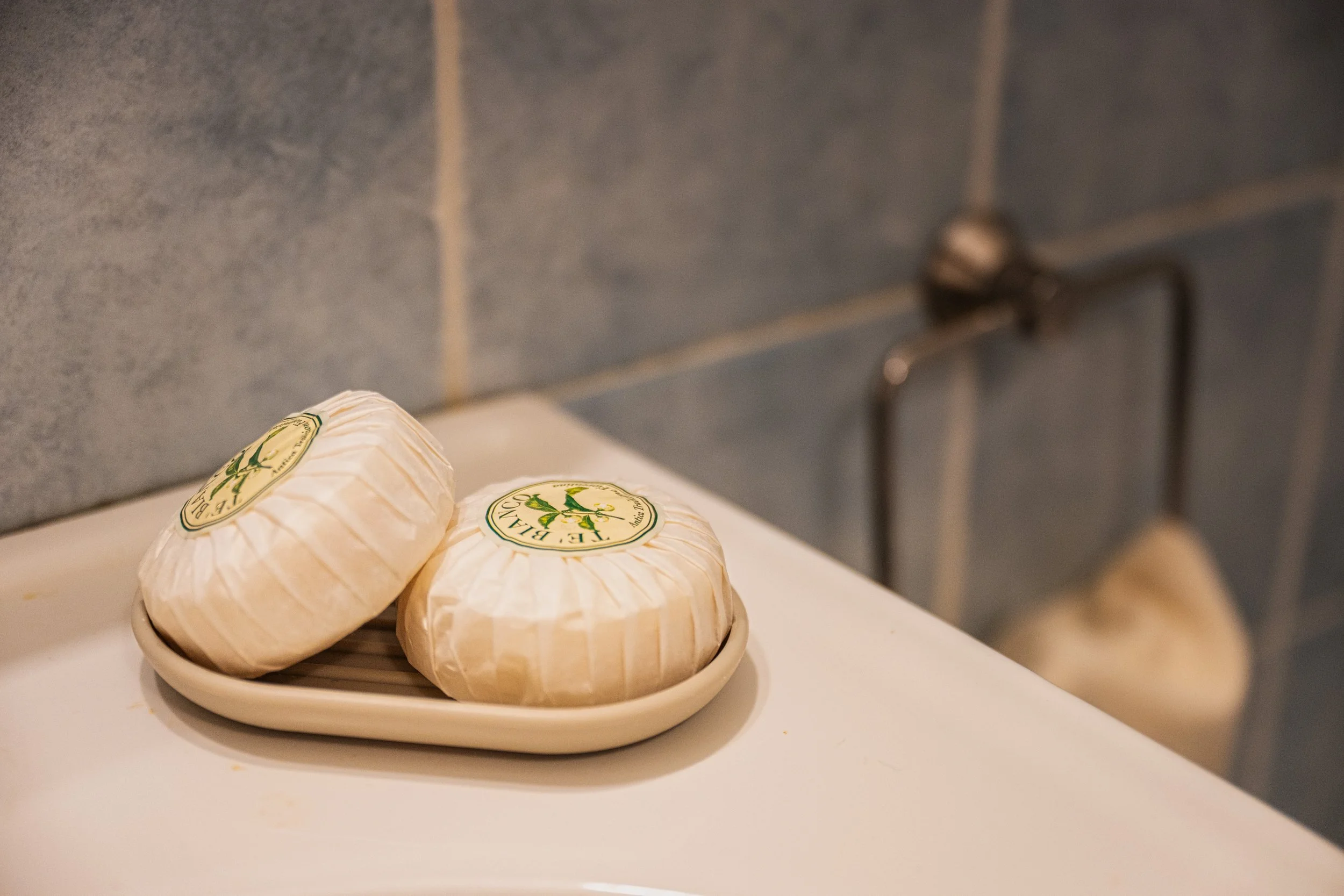 Formaggi avvolti in carta con etichetta verde, posti su un piatto bianco, in un ambiente con pareti di piastrelle grigie.