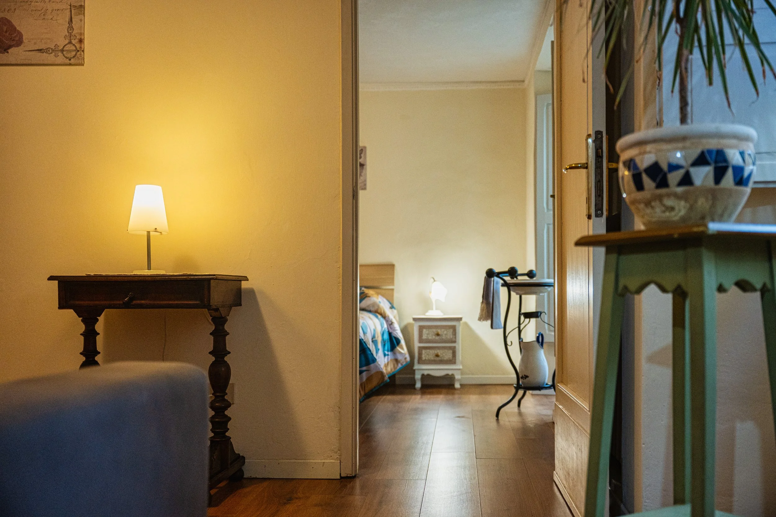 Vista dell'ingresso di una camera da letto con lampade accese, un comodino e un letto visibili nella stanza.