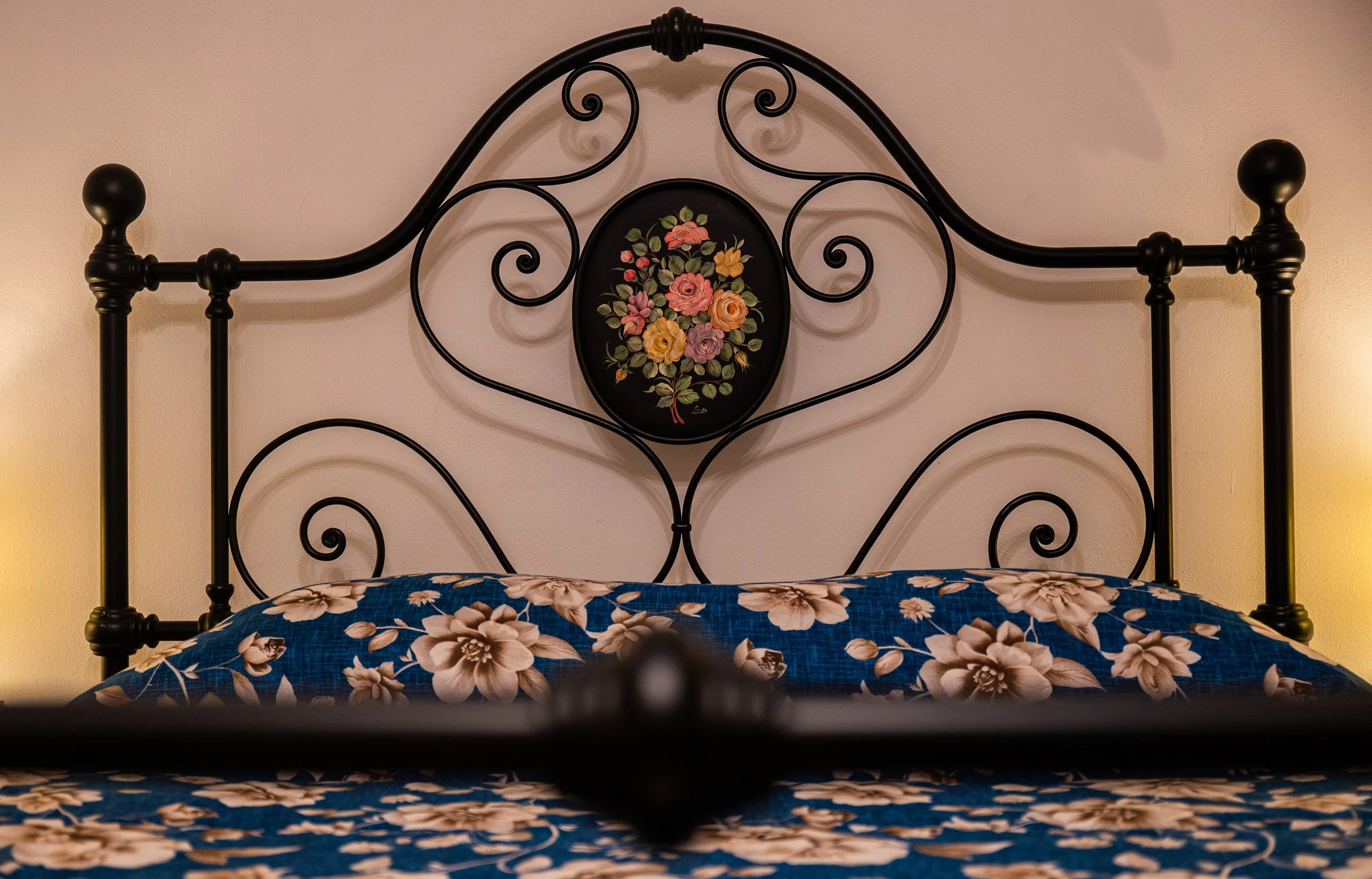testiera di ferro battuto con decorazione floreale e copriletto blu con fiori beige.