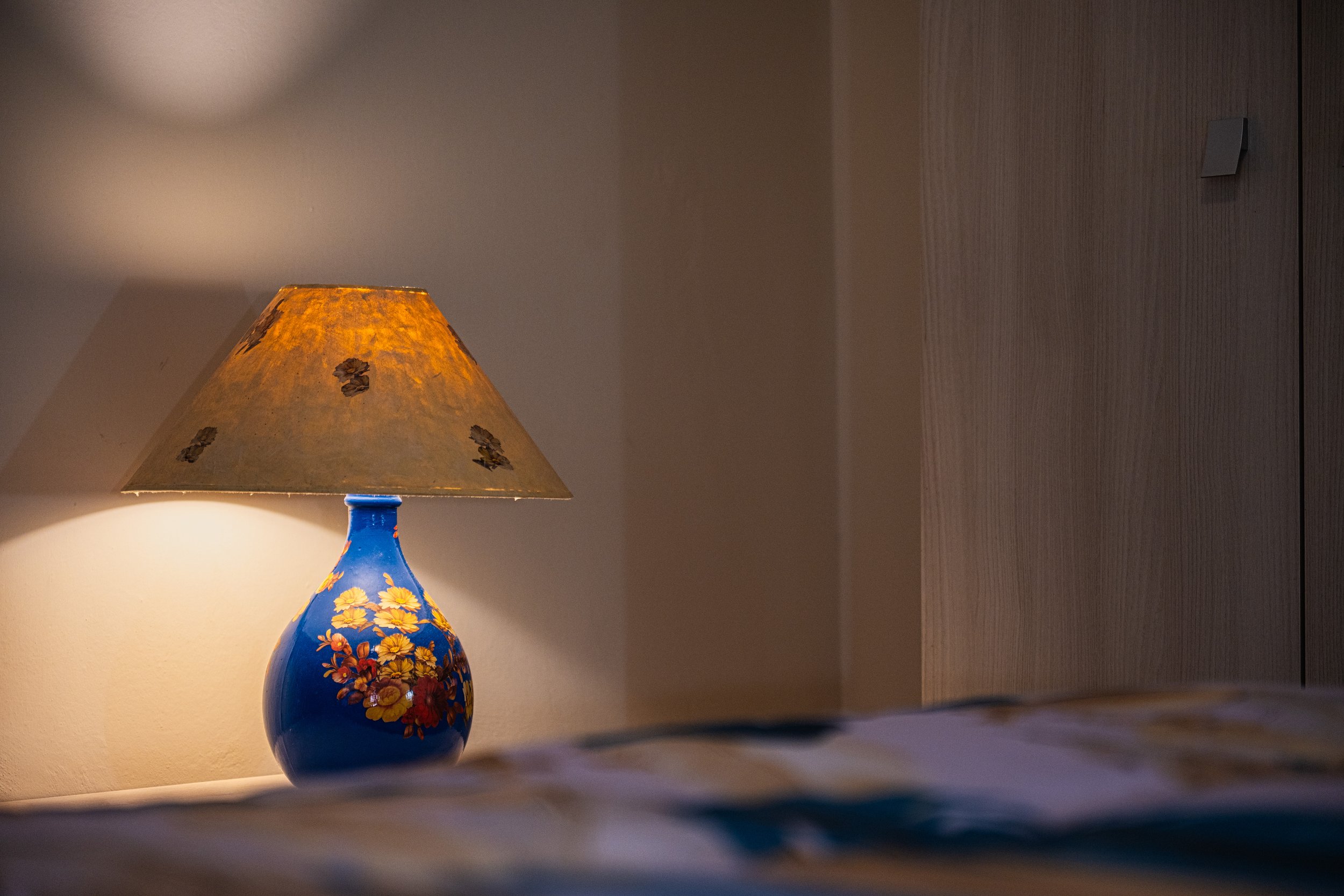 Lampi da tavolo colorato con base blu e decorazioni floreali, accanto a una parete di legno