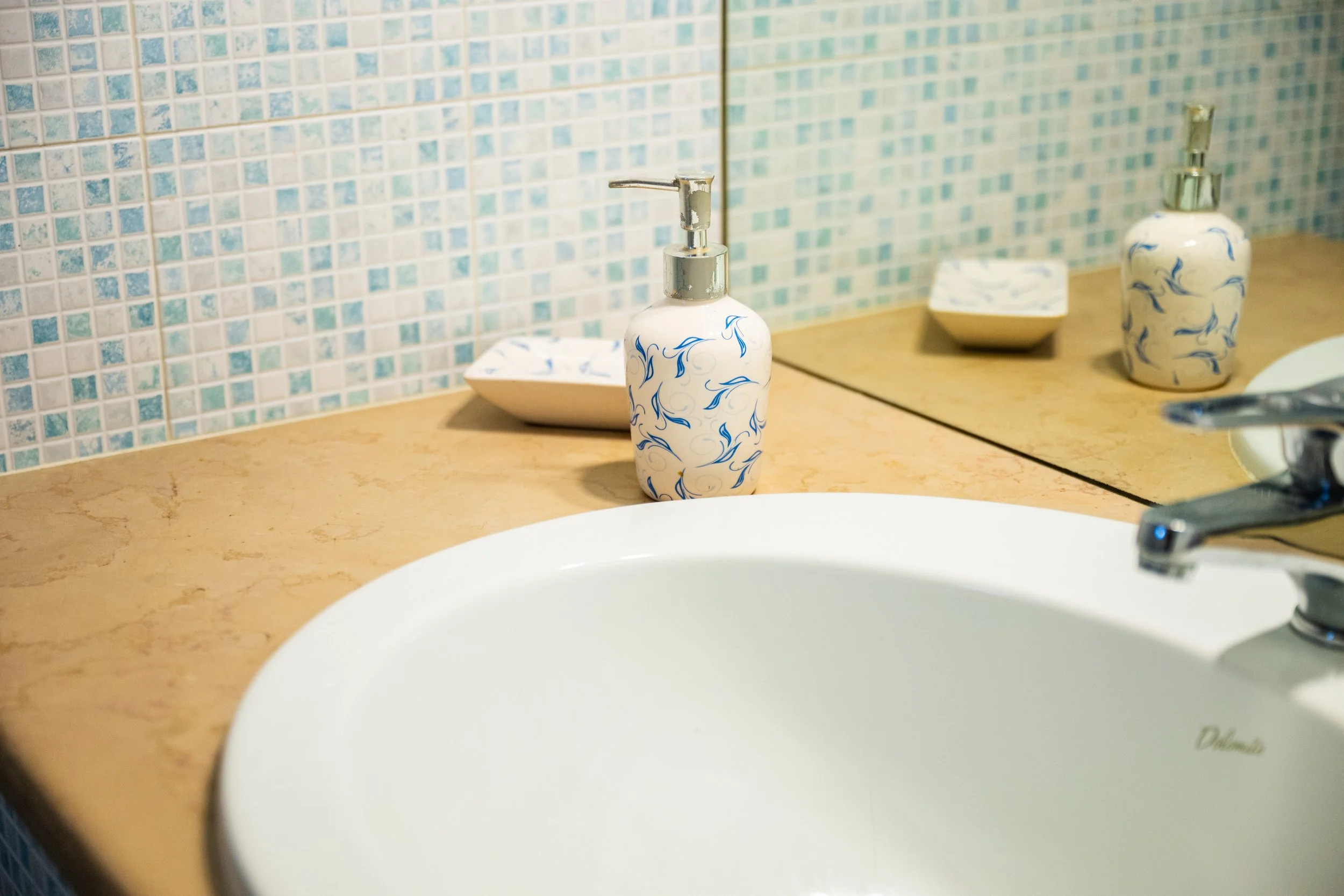 Vasca da bagno con piantana per sapone e una ciotola, tutti con decorazioni blu, sul piano del lavandino in un bagno con pareti di ceramica azzurra.