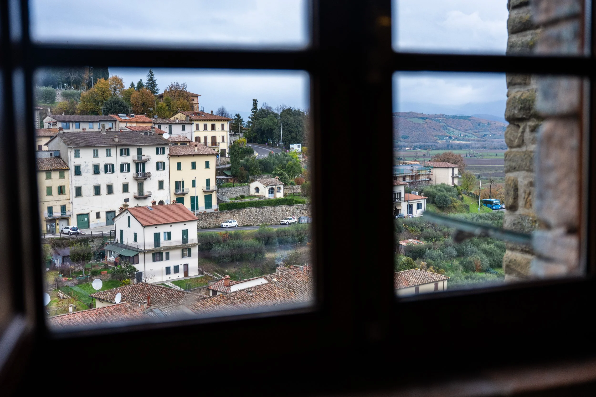 Vista di un villaggio con case colorate e colline sullo sfondo, vista attraverso una finestra con confine in legno e pietra.