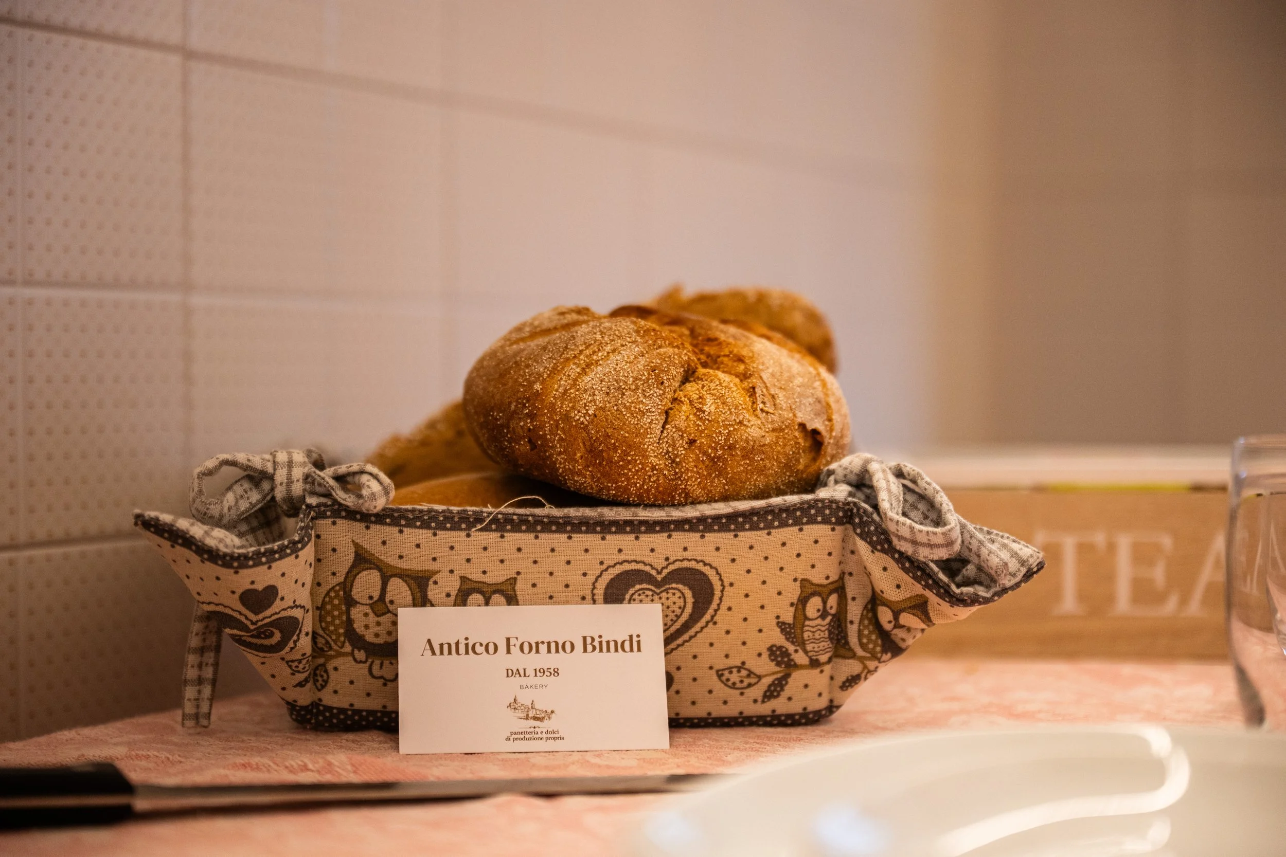 Pane artisanale in una cesta con un cartellino che dice 'Antico Forno Bindi DAL 1958' in una cucina.