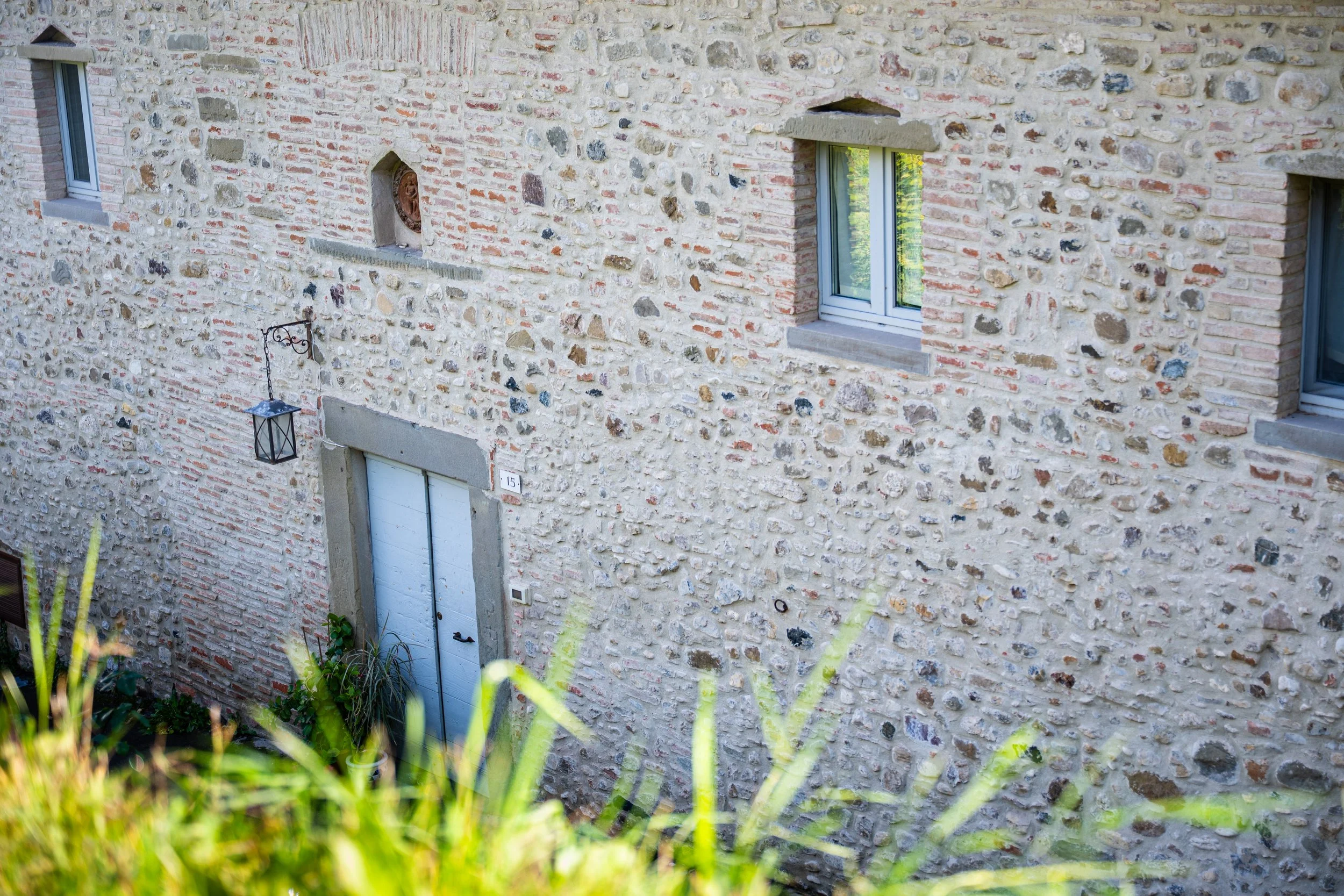 Facciata di una casa in pietra con finestre e porta, decorata con una lanterna appesa.