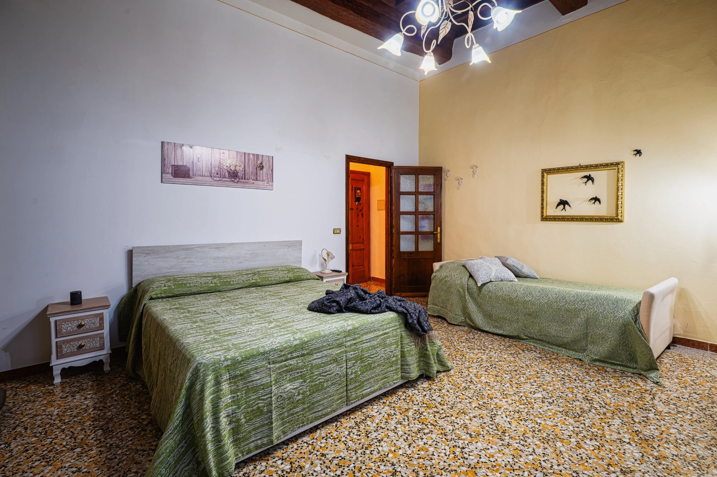 Camera da letto con due letti, uno matrimoniale e uno singolo, con copriletti verdi, un quadro sulla parete e un lampadario decorativo.